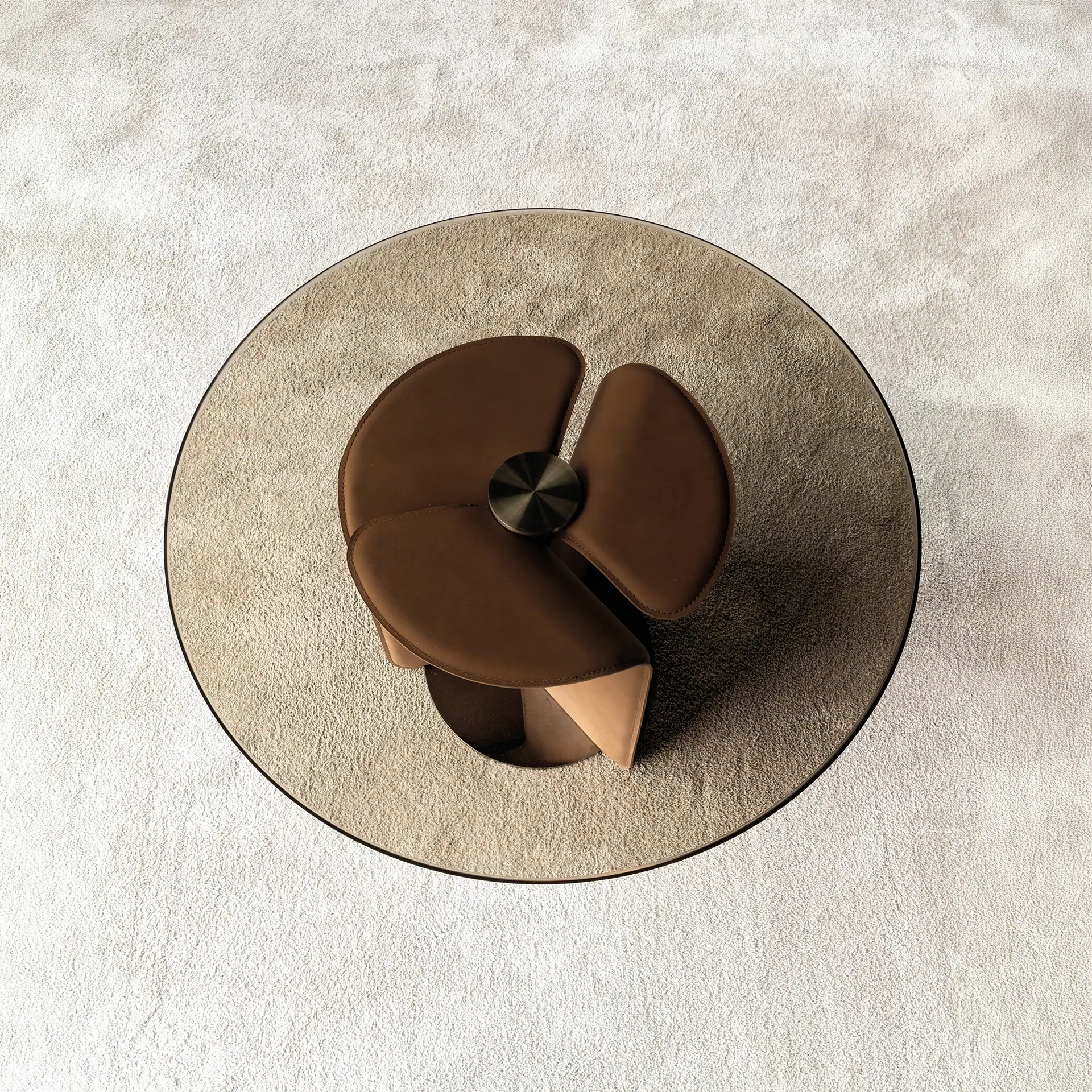 Overhead view of a round, smoky glass coffee table with a dark brown leather petal-shaped base on a light, textured rug.