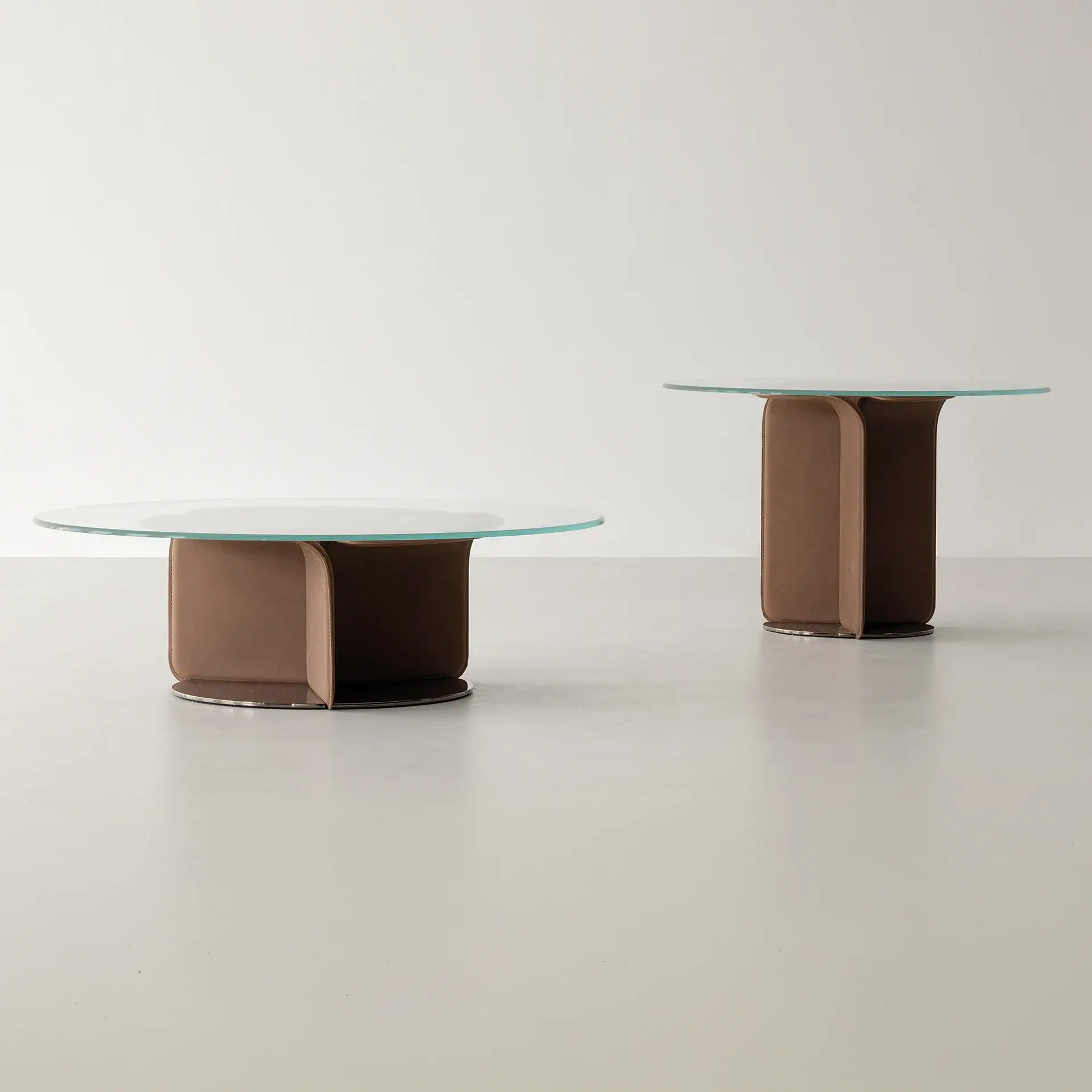 Two modern tables with round glass tops and brown sculptural bases. One is a low coffee table, the other a taller side table.