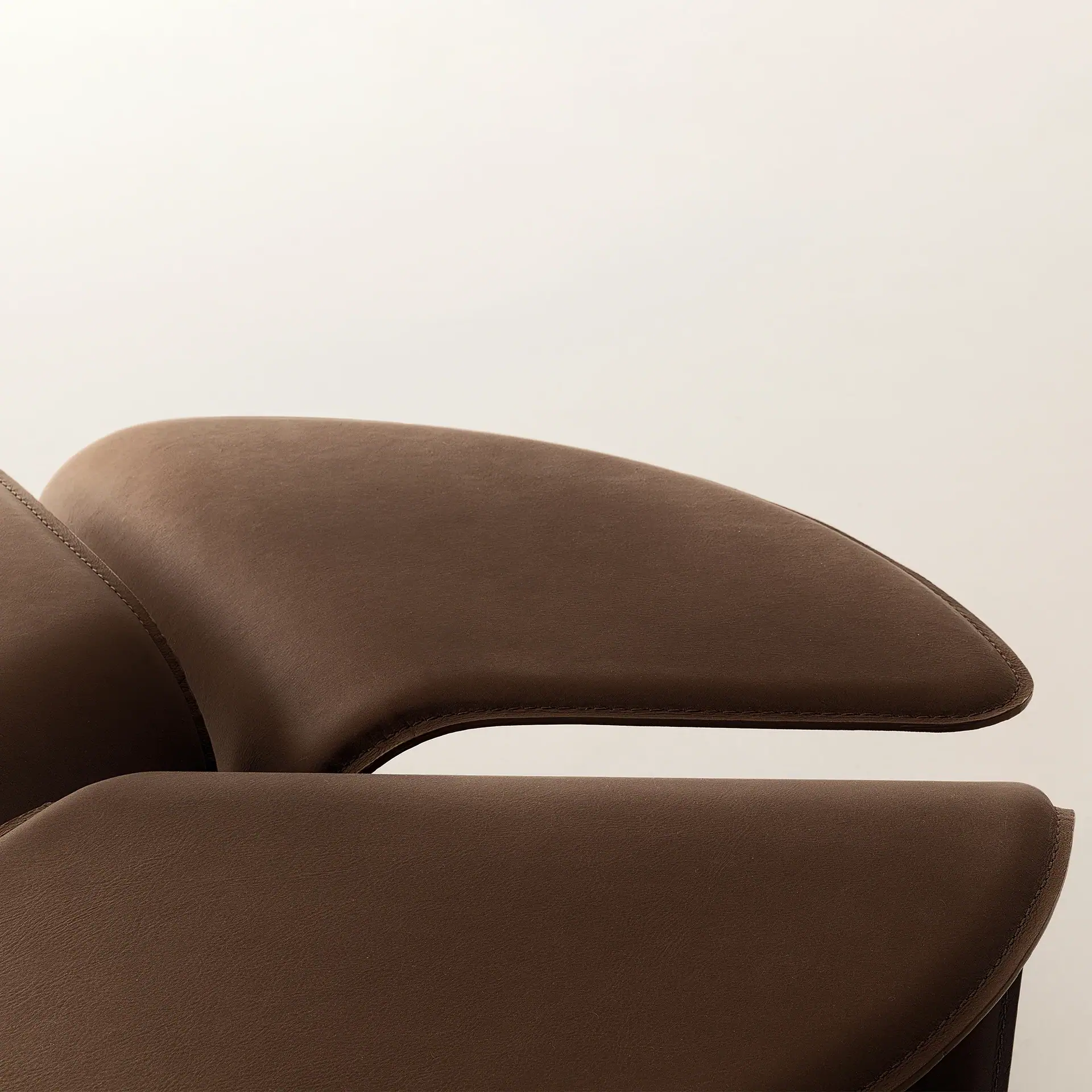 Close-up of curved, dark brown leather upholstery with visible stitching against a light background.