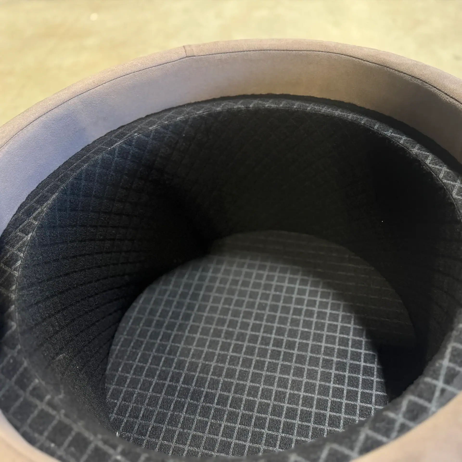 Overhead view of a circular object with a light brown rim and a dark gray interior lining featuring a light gray grid pattern.