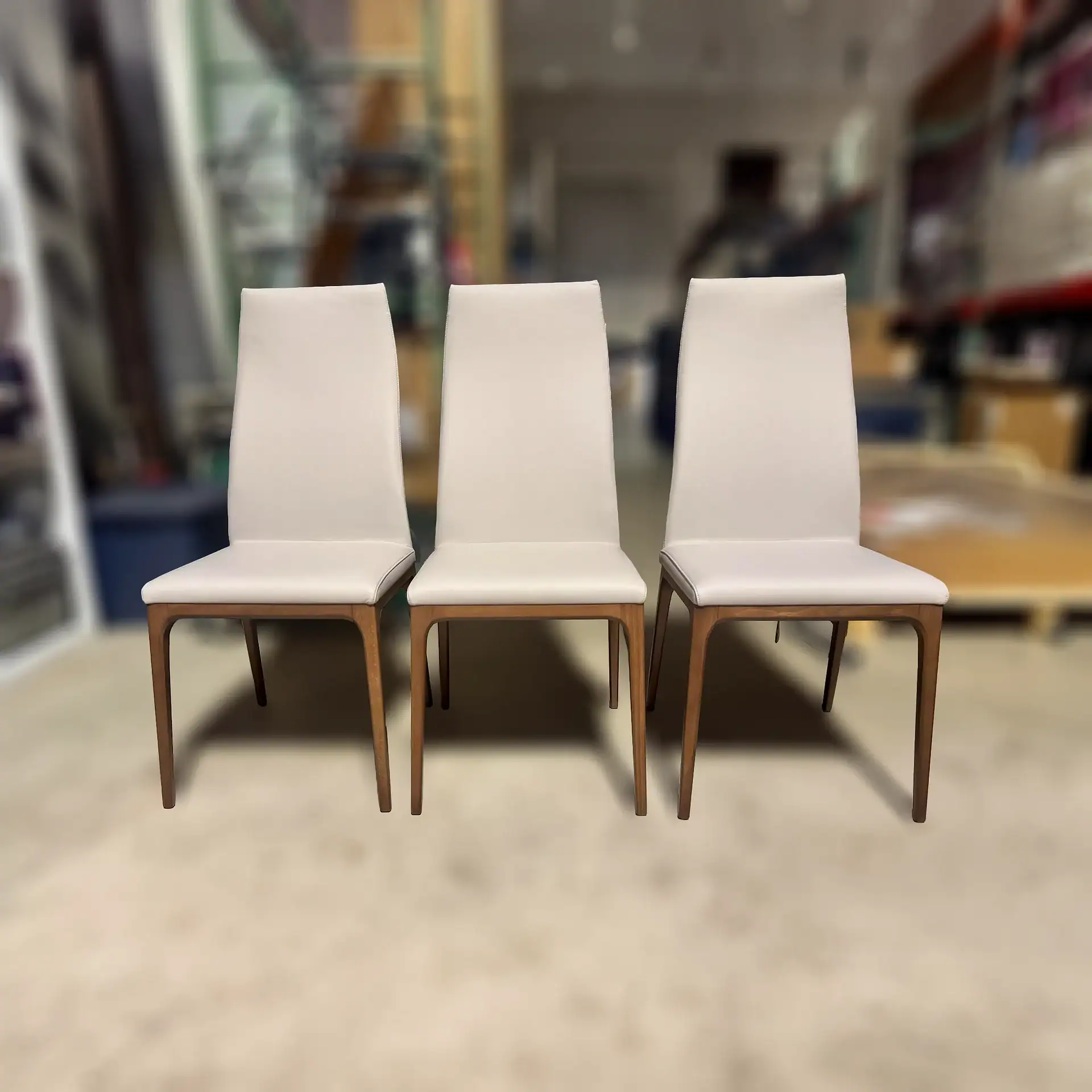 Three light beige upholstered dining chairs with dark wood frames arranged in a row.