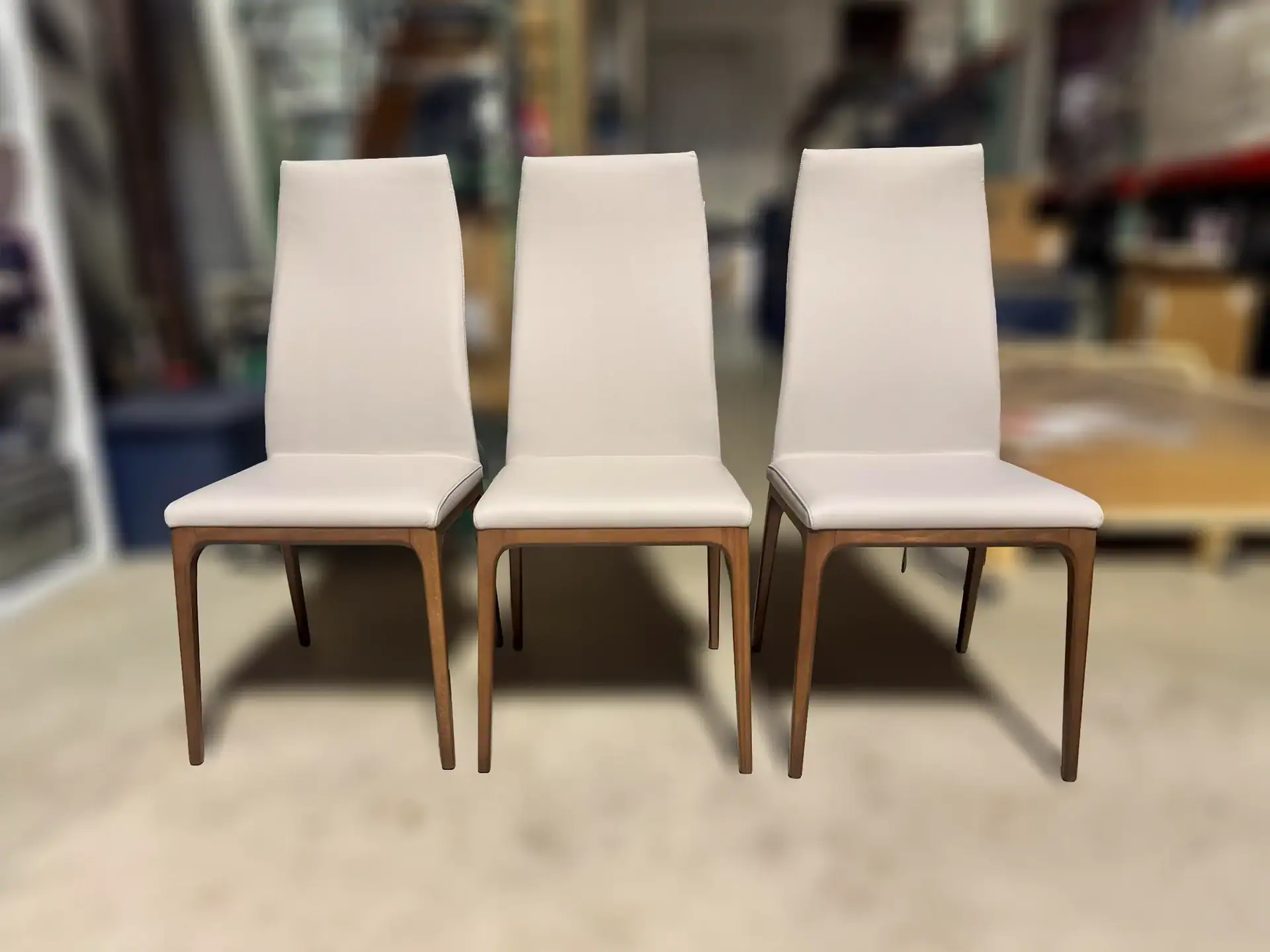 Three light-colored upholstered dining chairs with wooden frames arranged in a row.