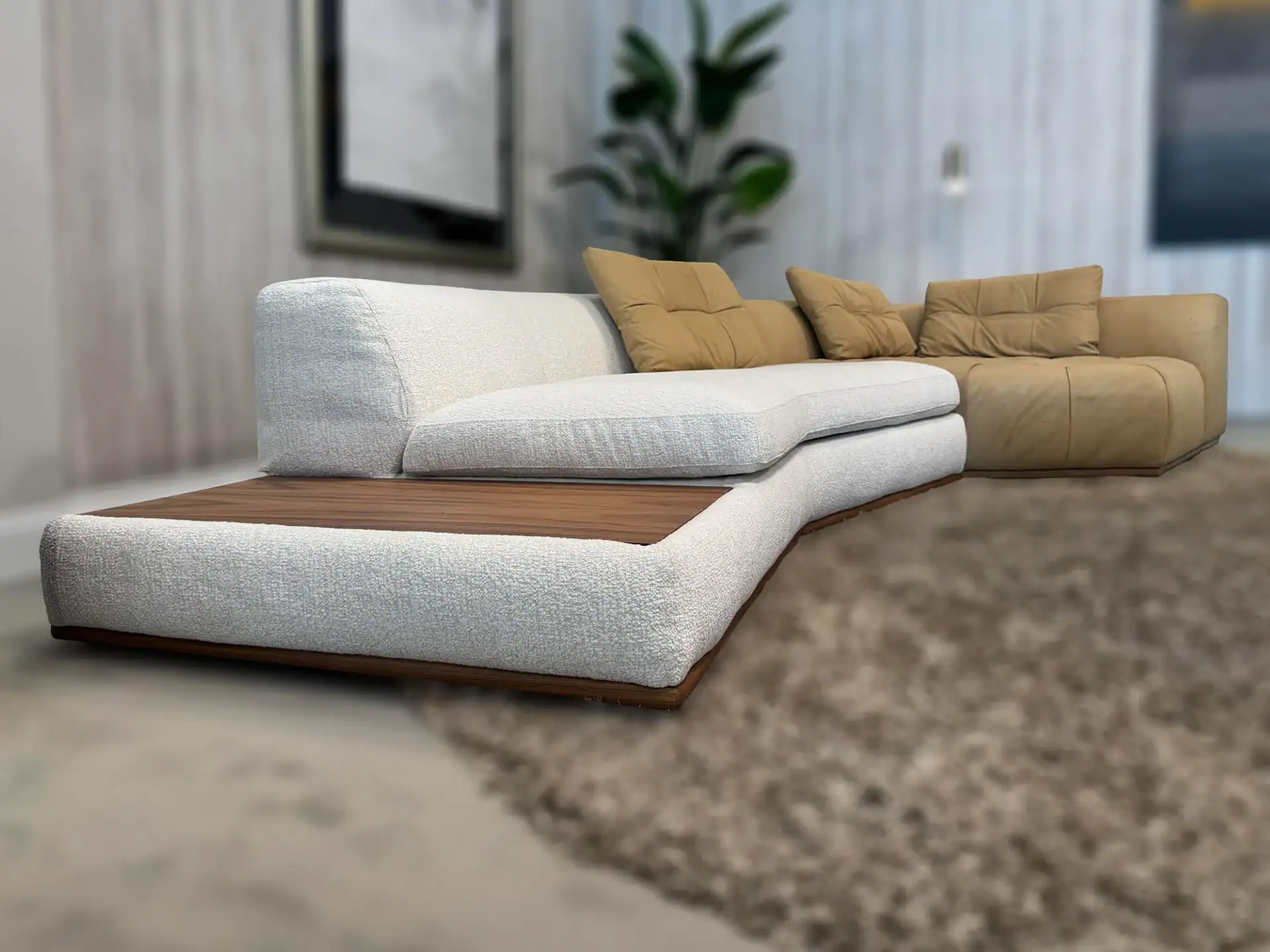 A modern L-shaped sectional sofa with an off-white fabric section featuring a wooden side panel, and a tan leather section, both with mustard-colored throw pillows, on a shaggy brown rug.