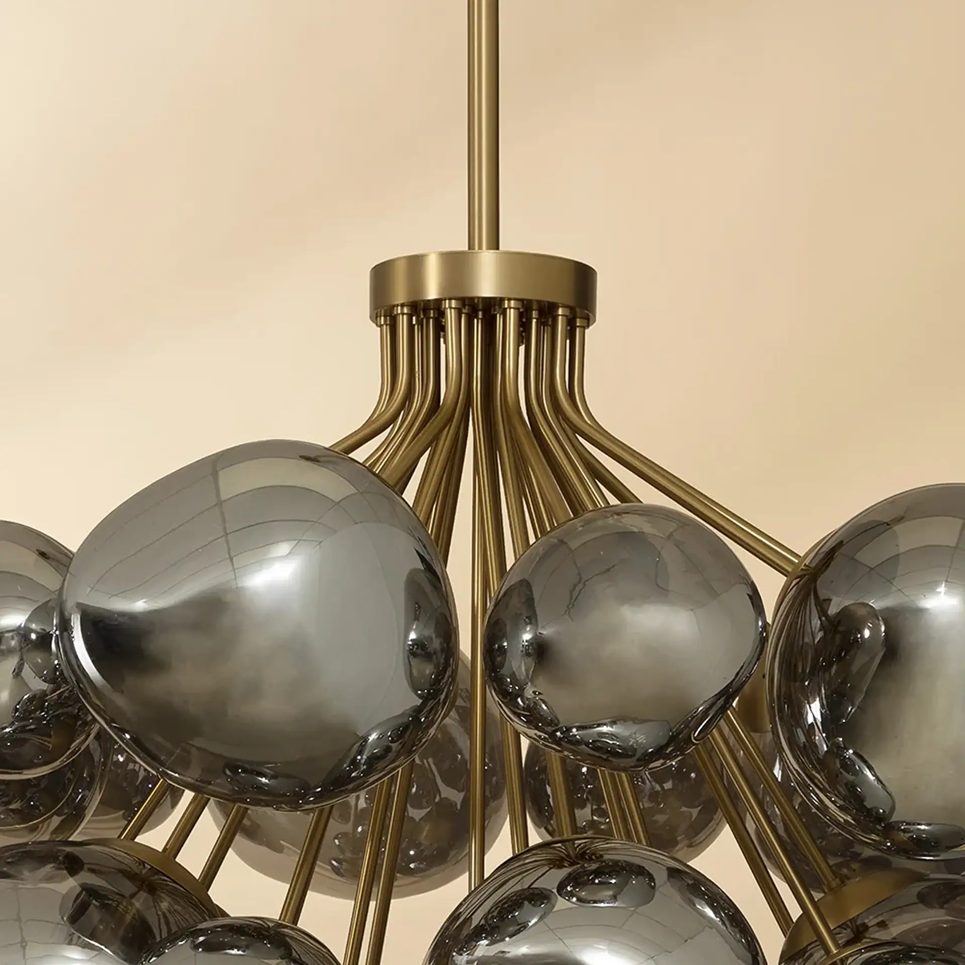 Close-up of a modern chandelier with a central brass stem, radiating brass arms, and multiple reflective, smoky grey glass spheres.