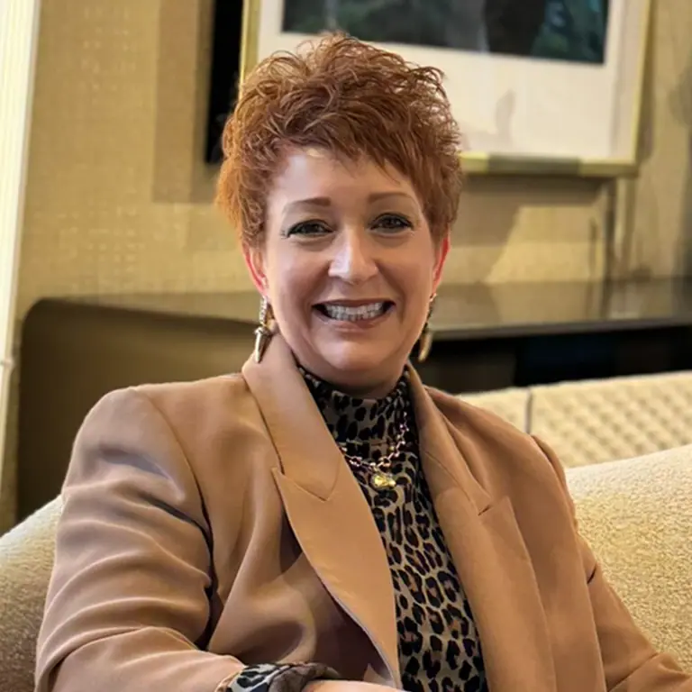 Deanna Martin seated on a beige sofa in a blazer and leopard print top.