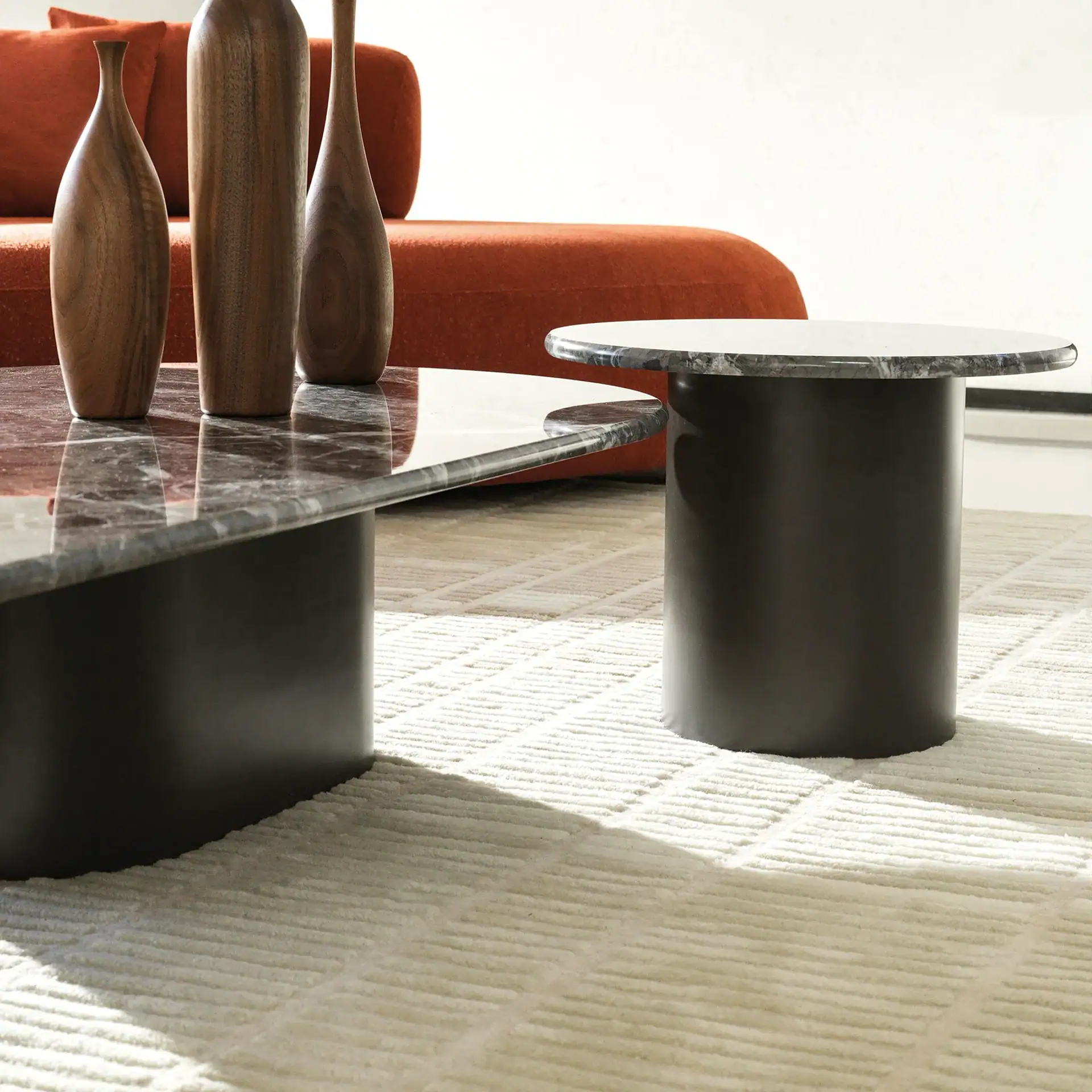 Modern living room with dark marble coffee and side tables, three wooden vases, an orange sofa, and a cream textured rug.