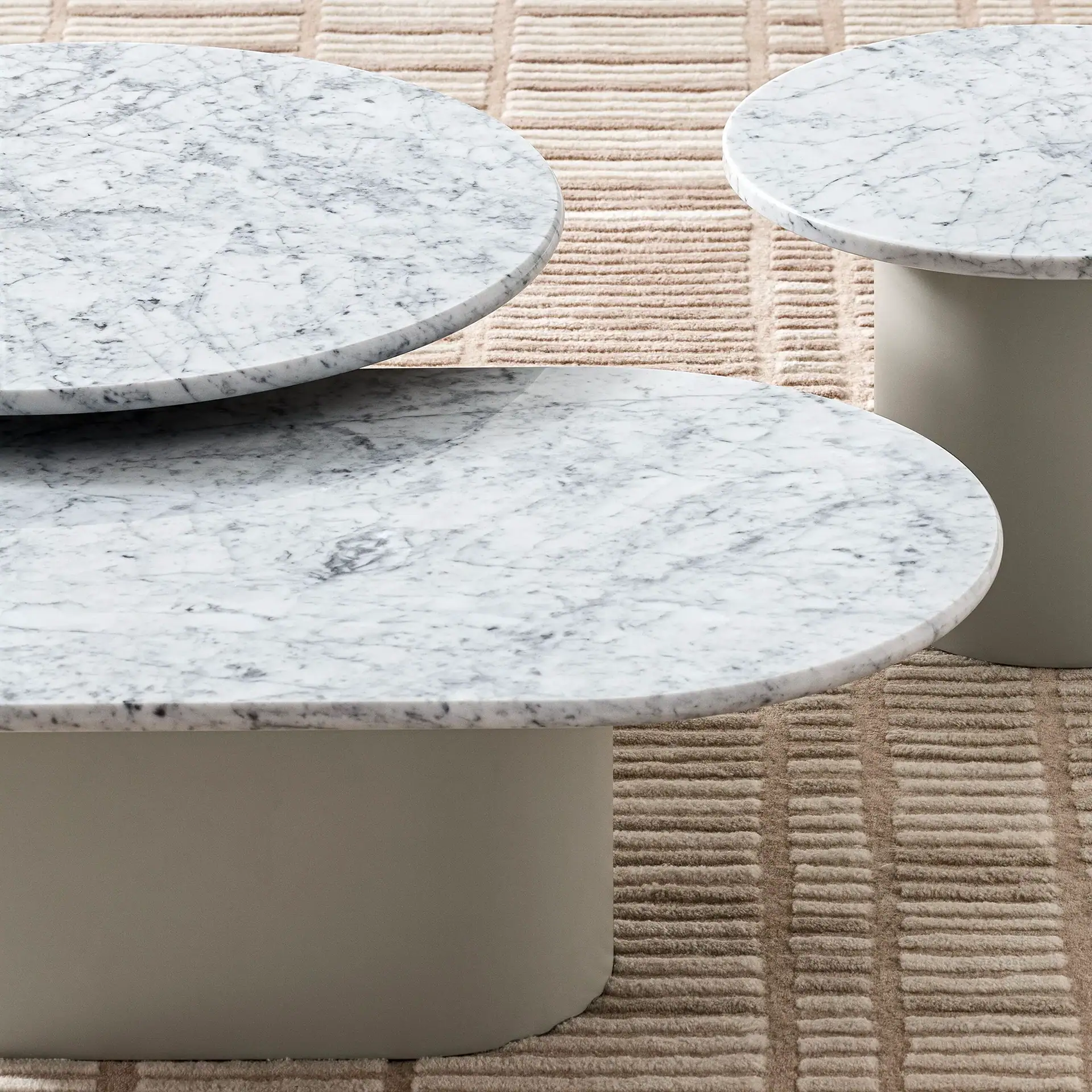 Three round coffee tables with white marble tops and grey bases on a beige textured rug.