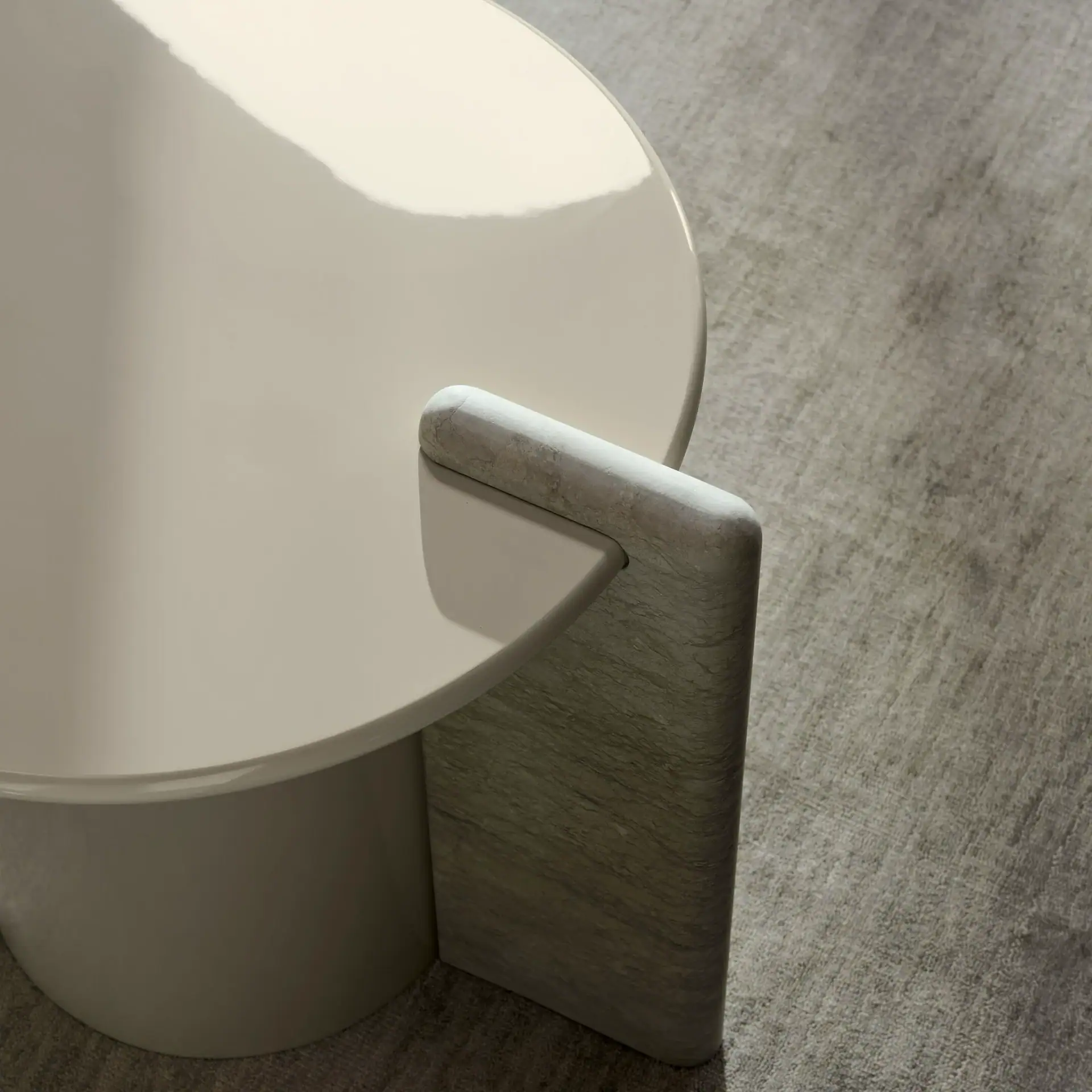 Close-up of a modern coffee table with a glossy cream circular top and a textured gray stone base on a gray rug.