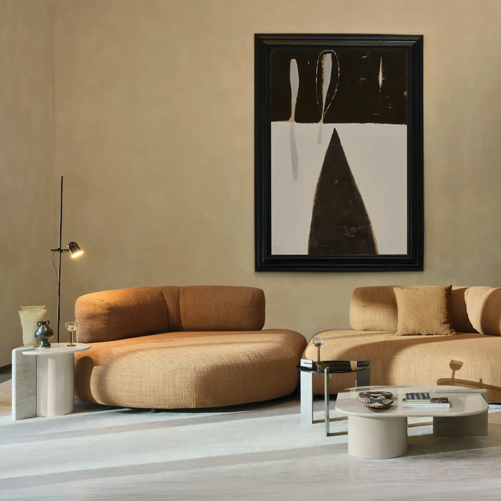 A modern living room with two tan modular sofas, a large abstract painting, a coffee table, and side tables with minimalist decor.