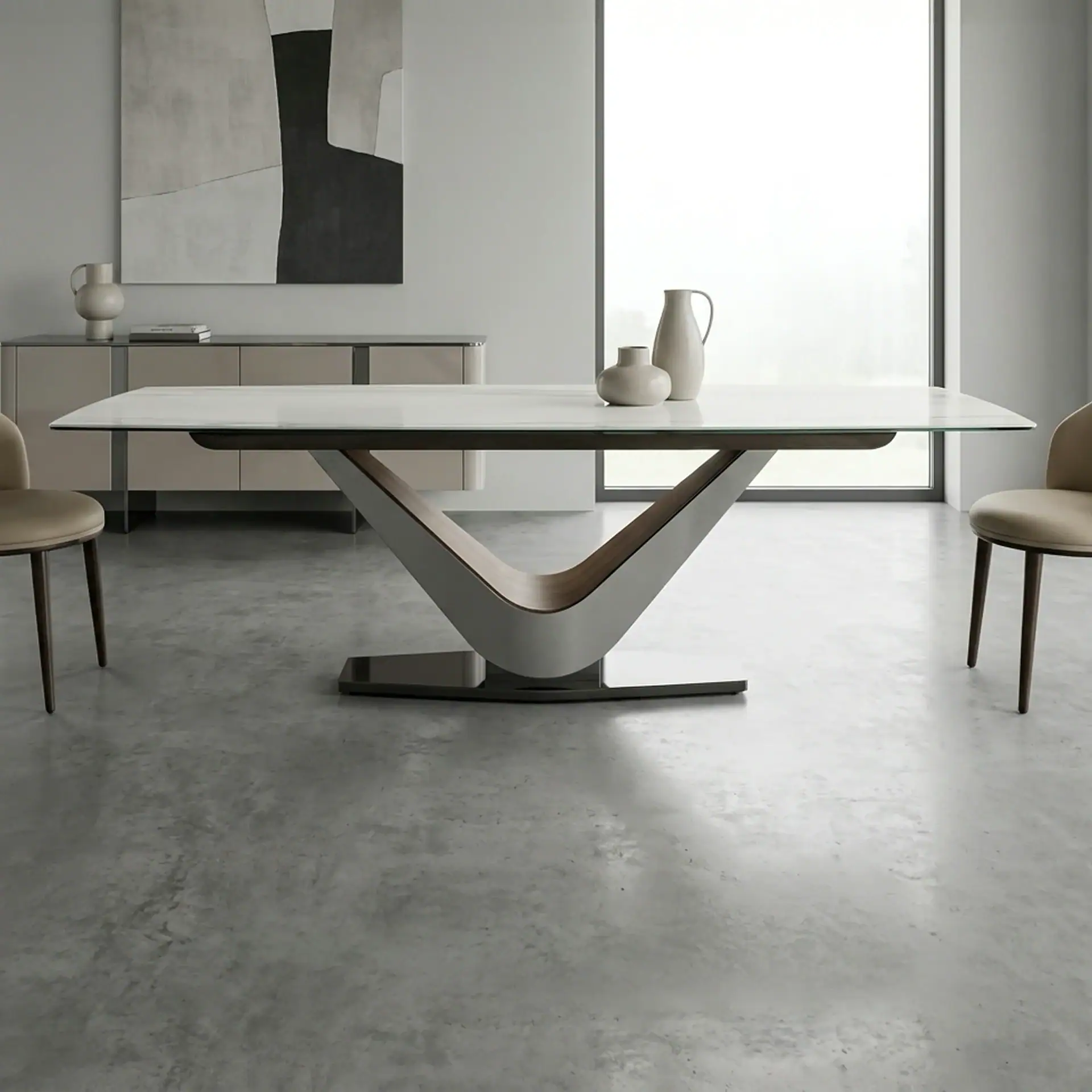 A modern dining room with a white-topped table, V-shaped silver and wood base, two beige chairs, and minimalist grey decor, including abstract art and vases.