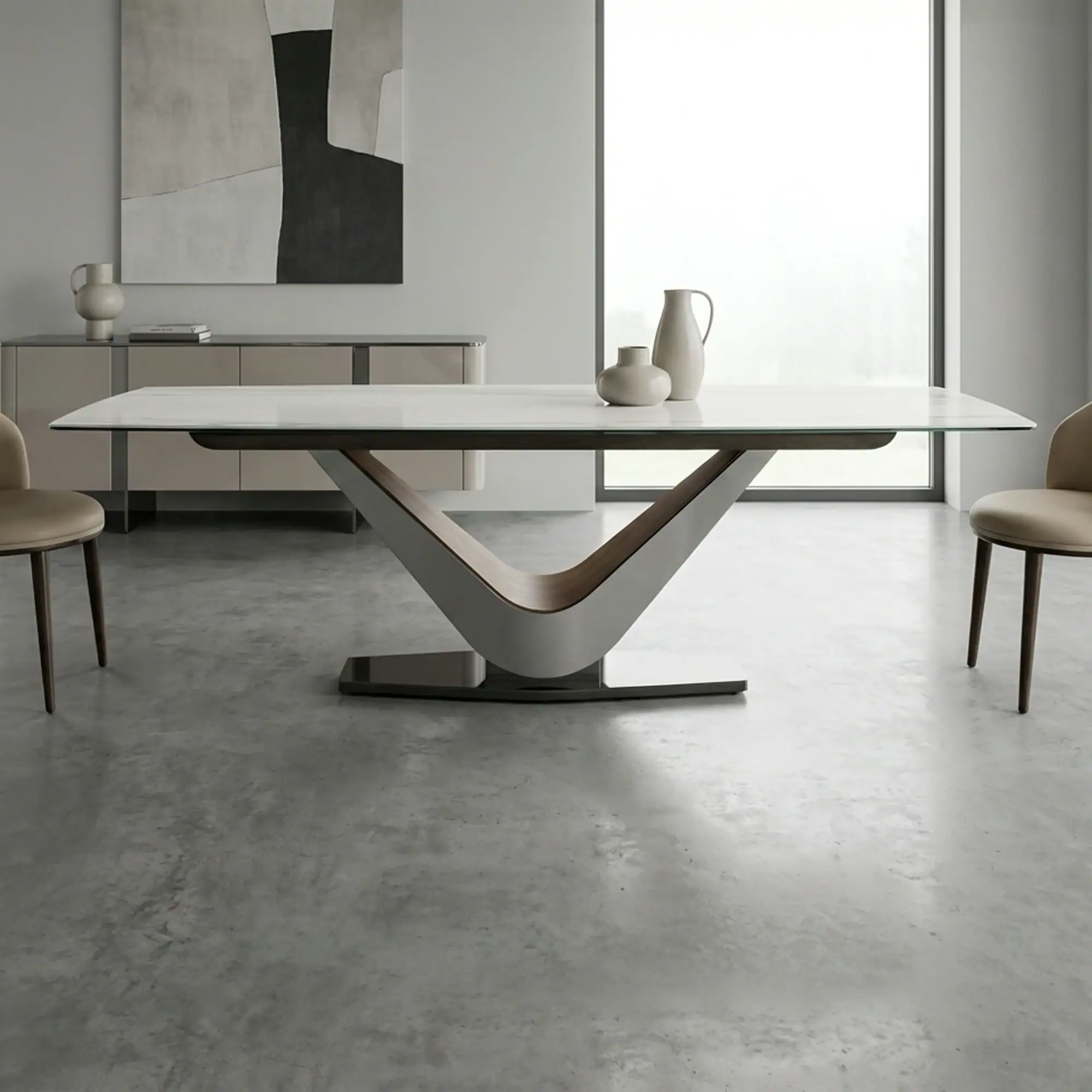 A modern dining room with a white-topped table, V-shaped silver and wood base, two beige chairs, and minimalist grey decor, including abstract art and vases.