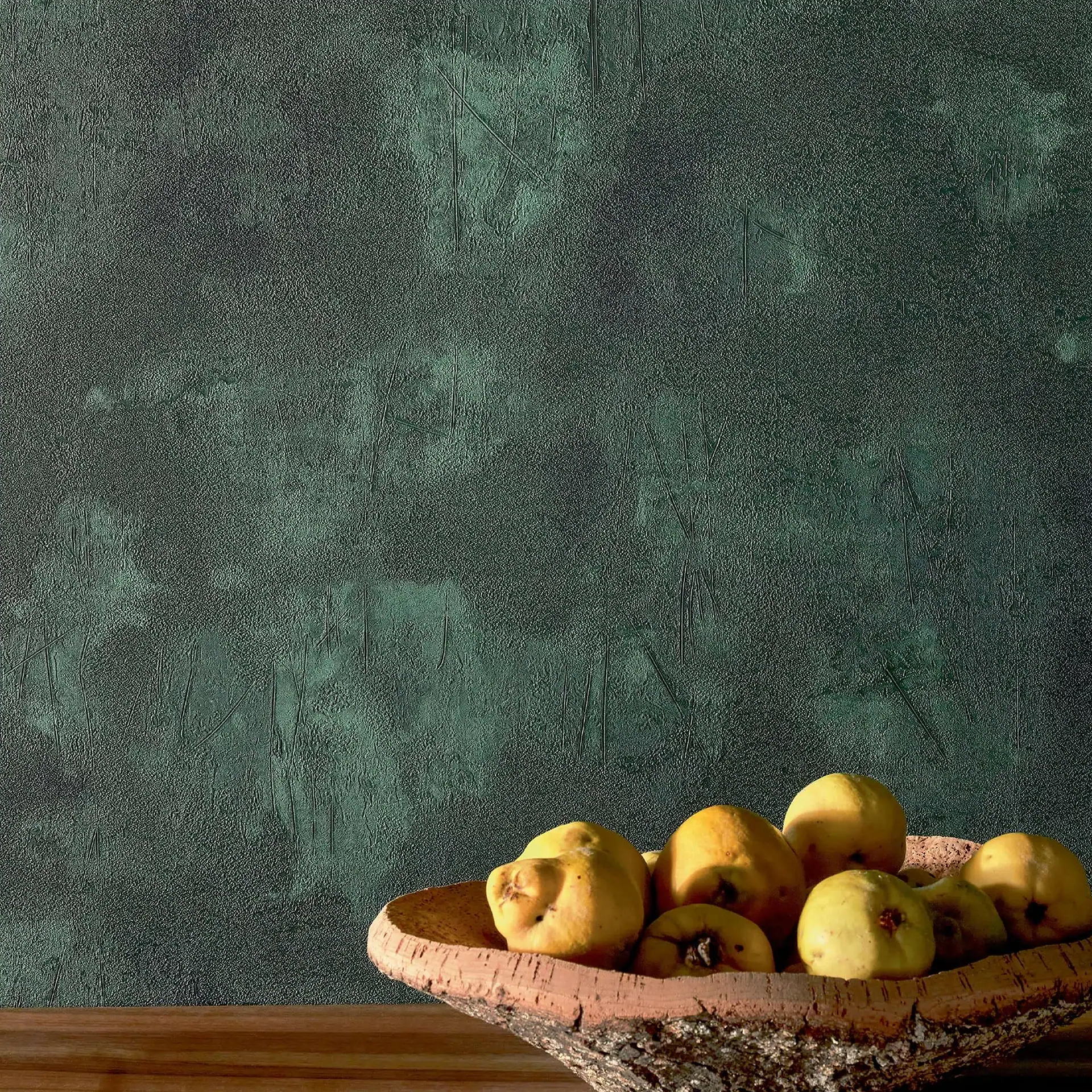 A rustic bark bowl filled with pale yellow quinces sits on a wooden surface against a dark green textured wall.
