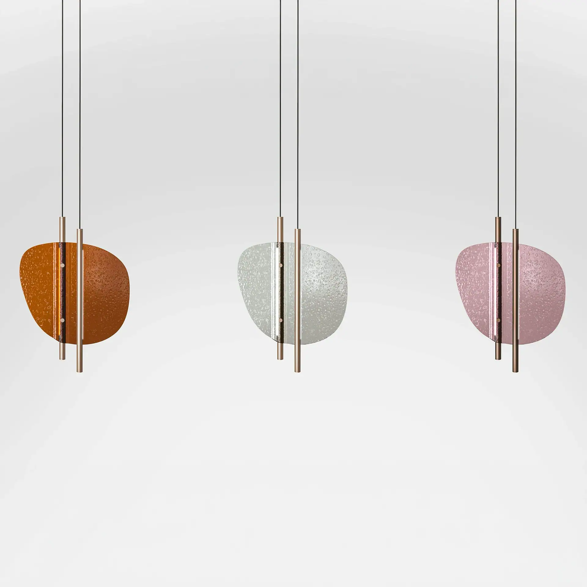 Three modern pendant lights with textured, irregularly shaped glass panels in amber, white, and pink, suspended by rose gold rods.