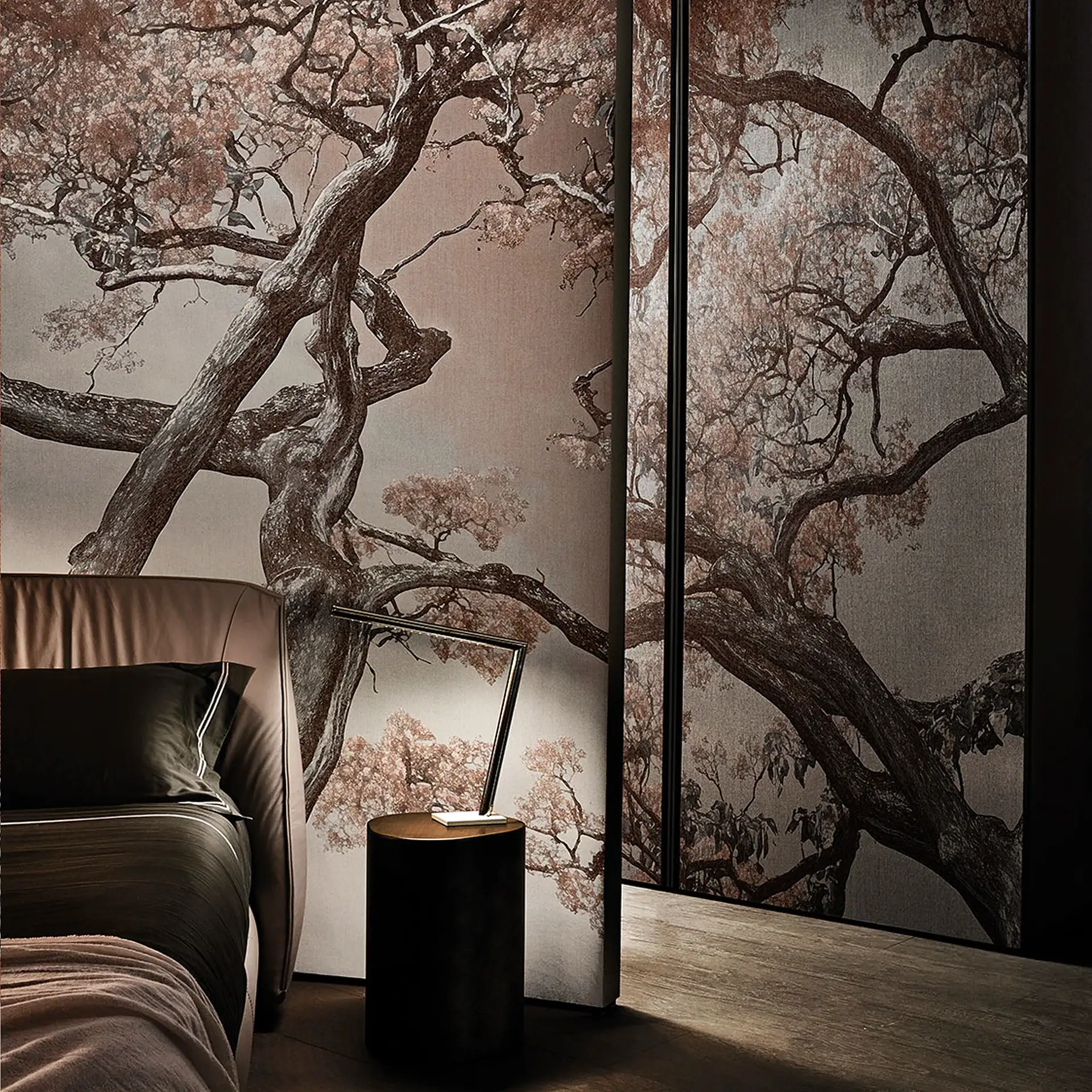 A modern bedroom with a large wall mural depicting a tree with reddish-brown leaves, a bed with dark bedding, and a dark nightstand with a lamp.