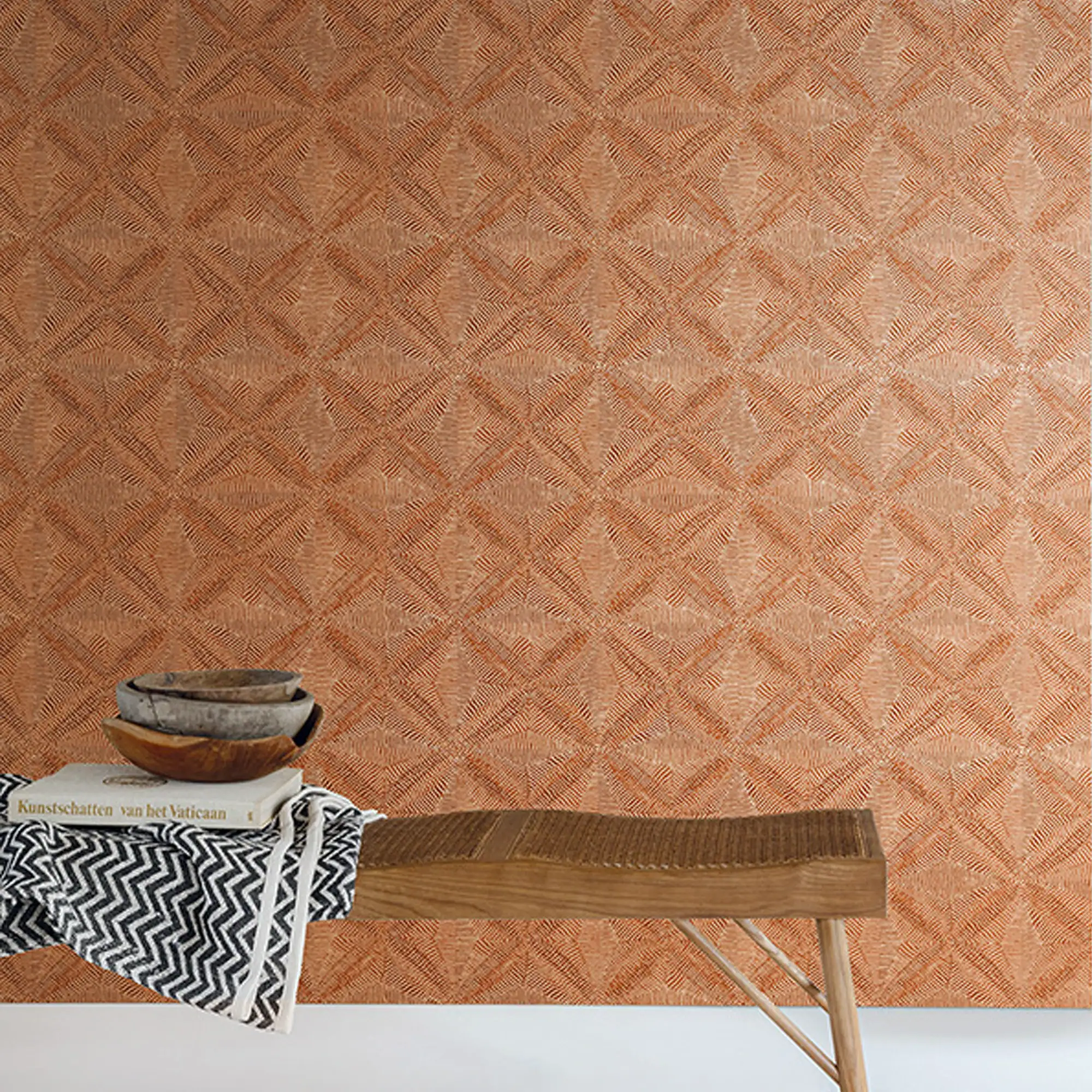 A wooden bench with a black and white patterned blanket, a book, and stacked bowls, set against a textured orange-brown geometric wallpaper.