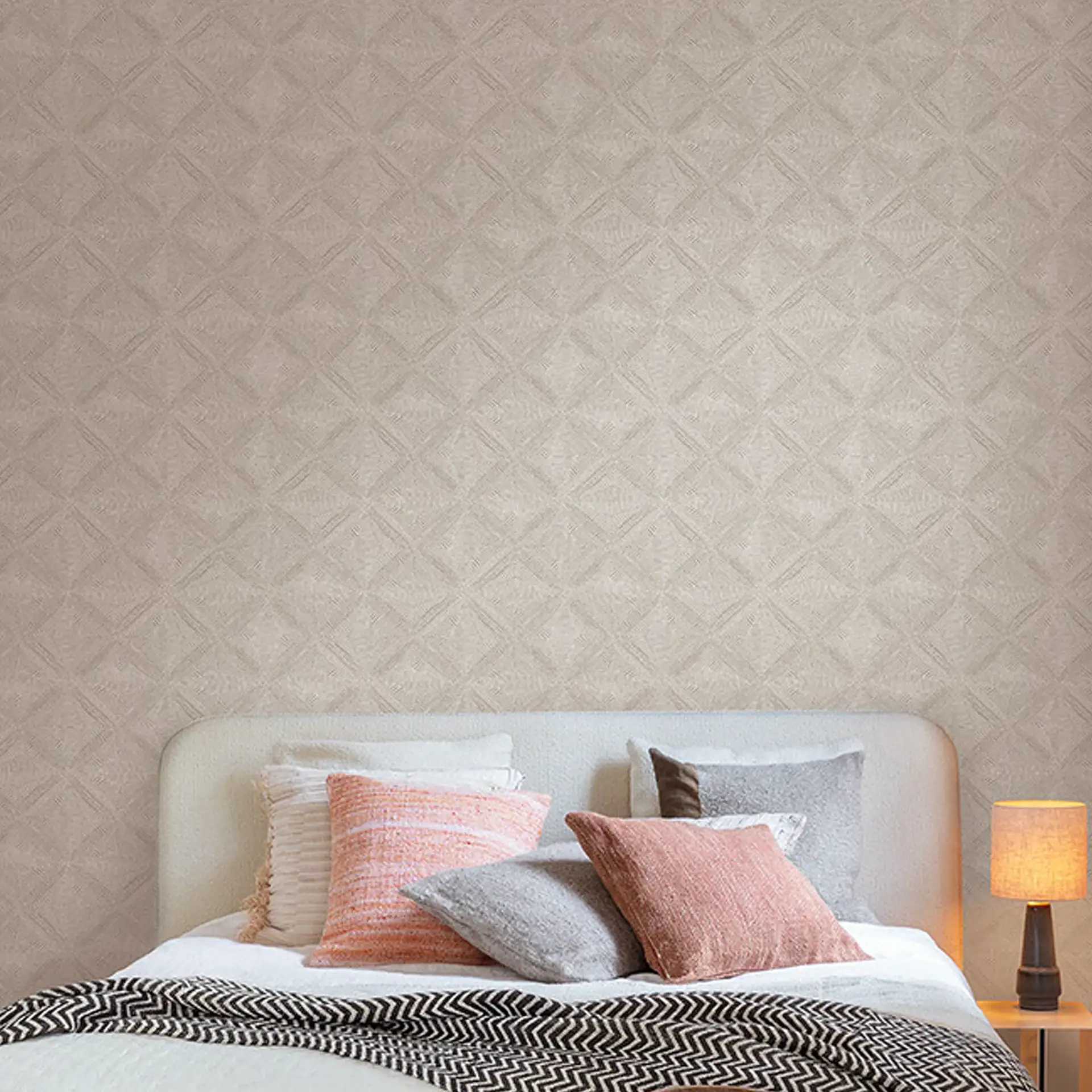 A bedroom with a bed, pillows, and a lamp against a light beige geometric patterned wallpaper.