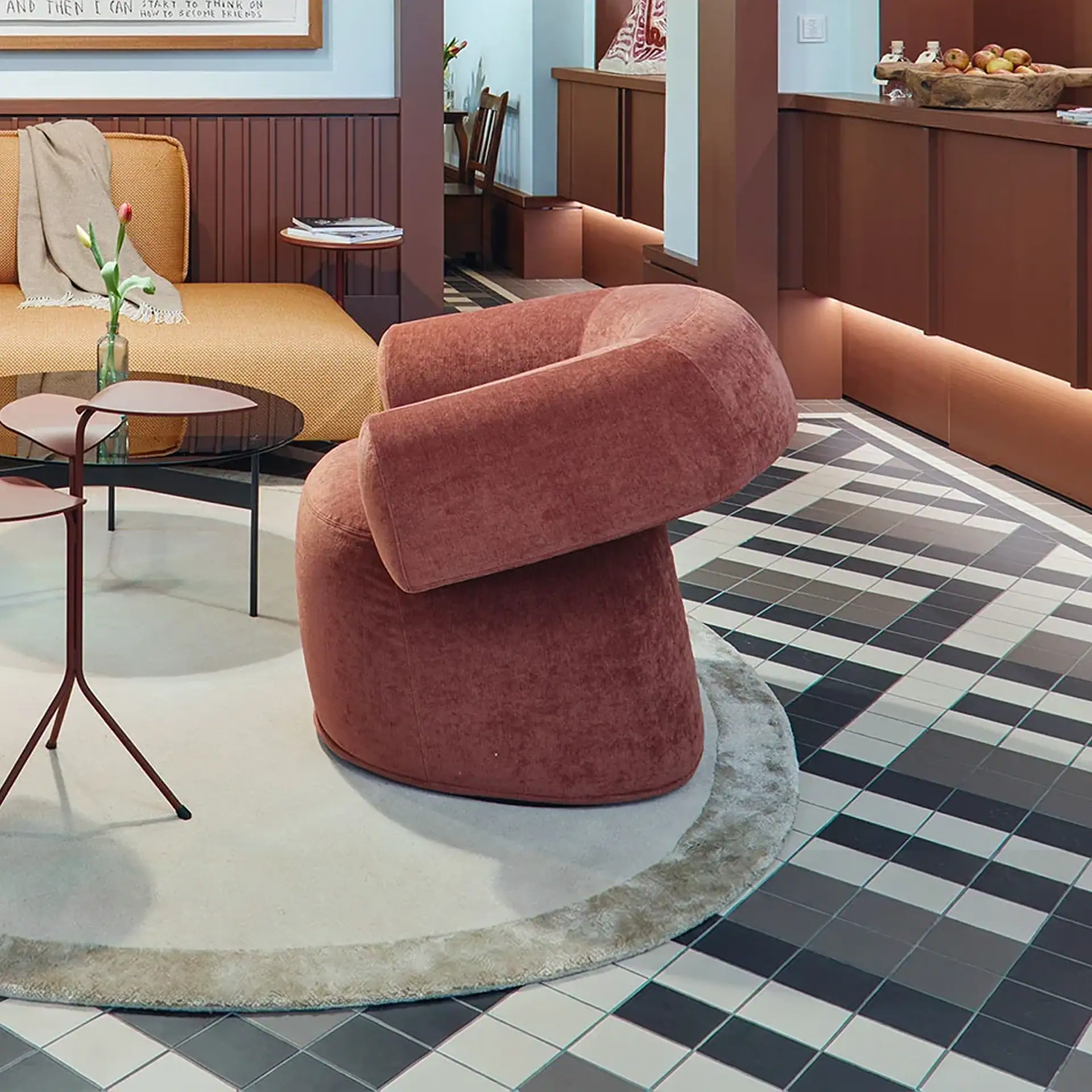 An interior living room with a dusty rose velvet armchair, a mustard yellow sofa, and a black, grey, and white geometric tiled floor.