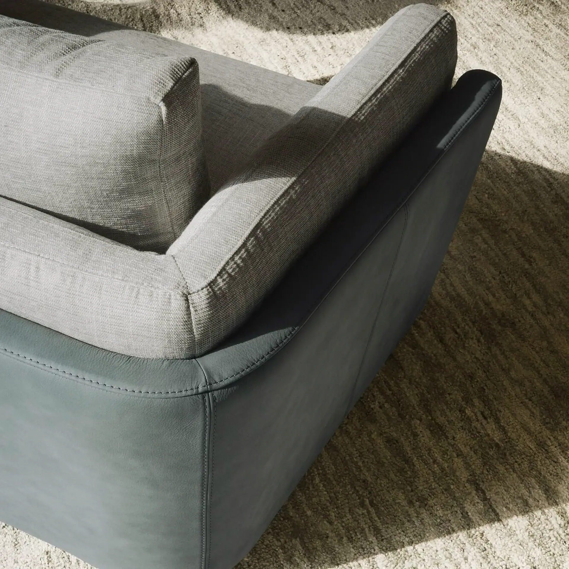 Overhead view of a two-toned sofa with light grey fabric cushions and dark bluish-grey leather base, on a light textured rug.