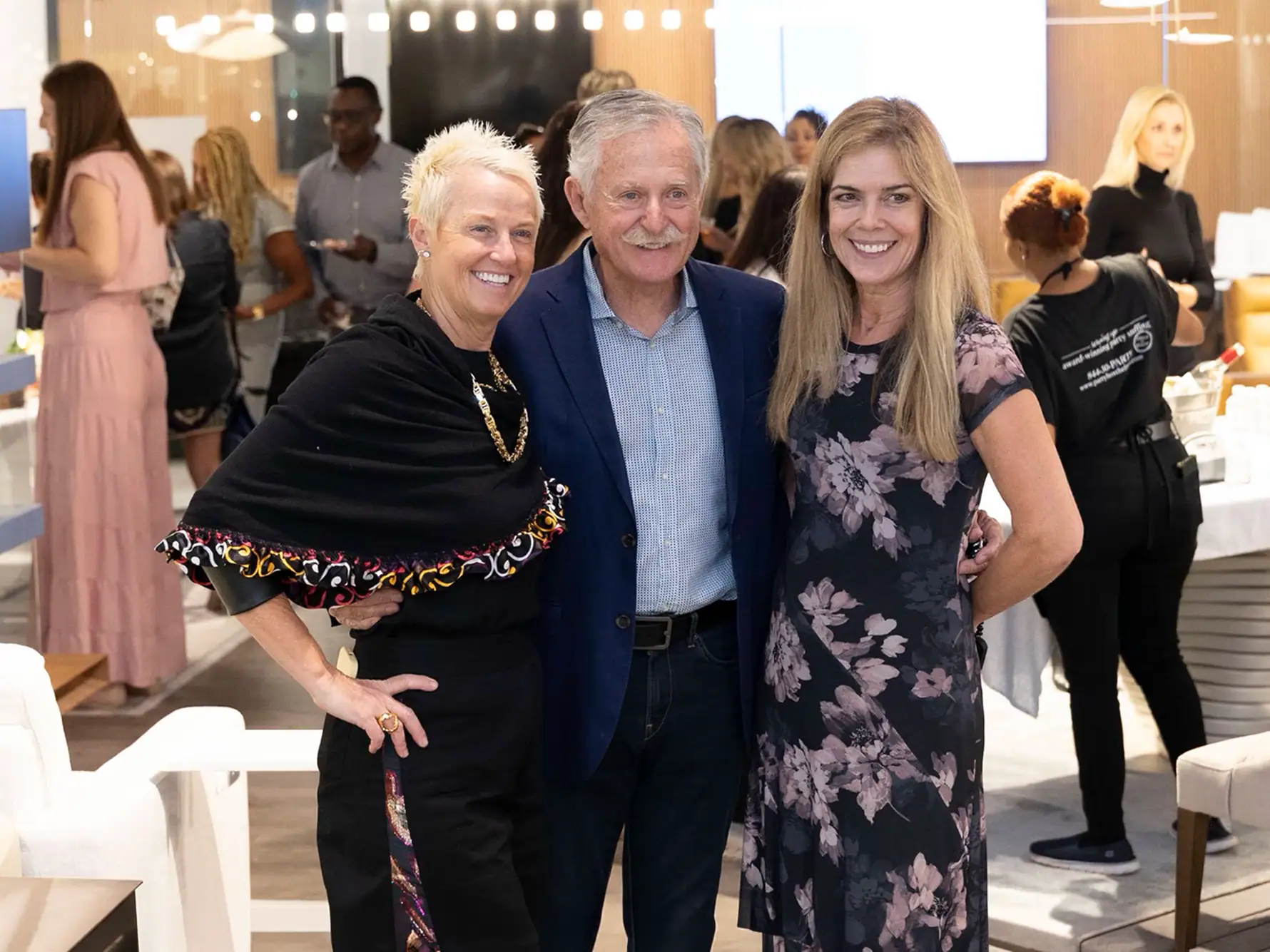 our core values demonstrate gratitude 1.2 | Sklar Furnishings Five women and one young girl smiling and looking at prints at an indoor event.