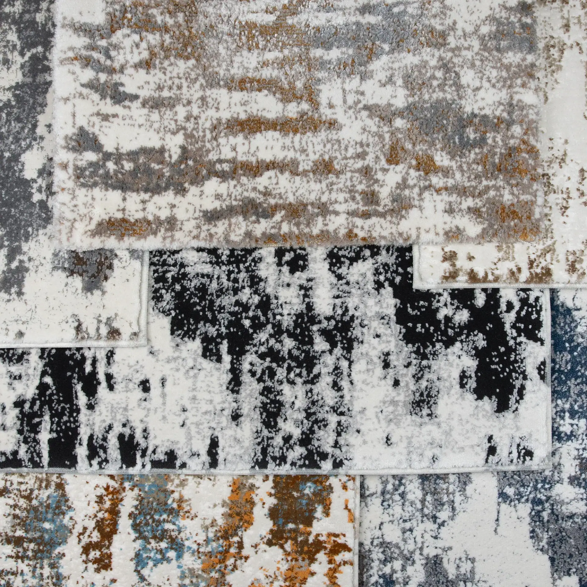 Close-up of overlapping rug samples with abstract, distressed patterns in white, gray, black, brown, and blue.