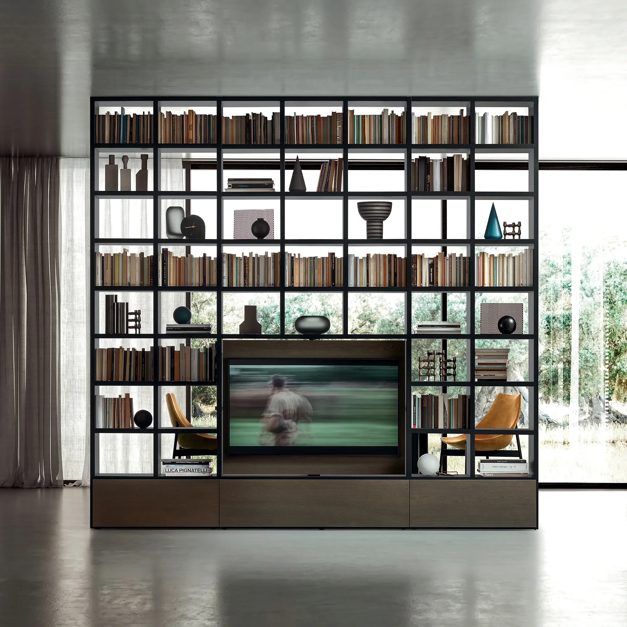 A large, black framed shelving unit with a built-in TV, filled with books and decor, in a modern room with concrete floors and large windows.