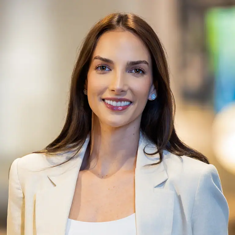 Headshot of a smiling young woman with long dark hair, wearing a light blazer and stud earrings.