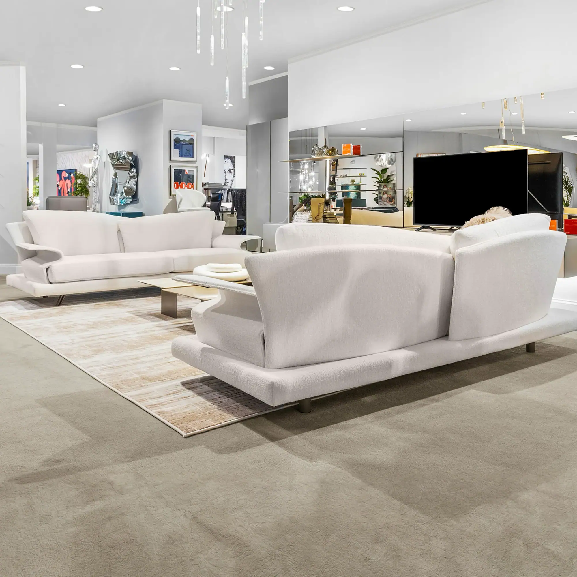 A modern living room with two white sofas, a glass coffee table, and an abstract rug on a gray carpet. Contemporary art and a large TV are visible in the background.