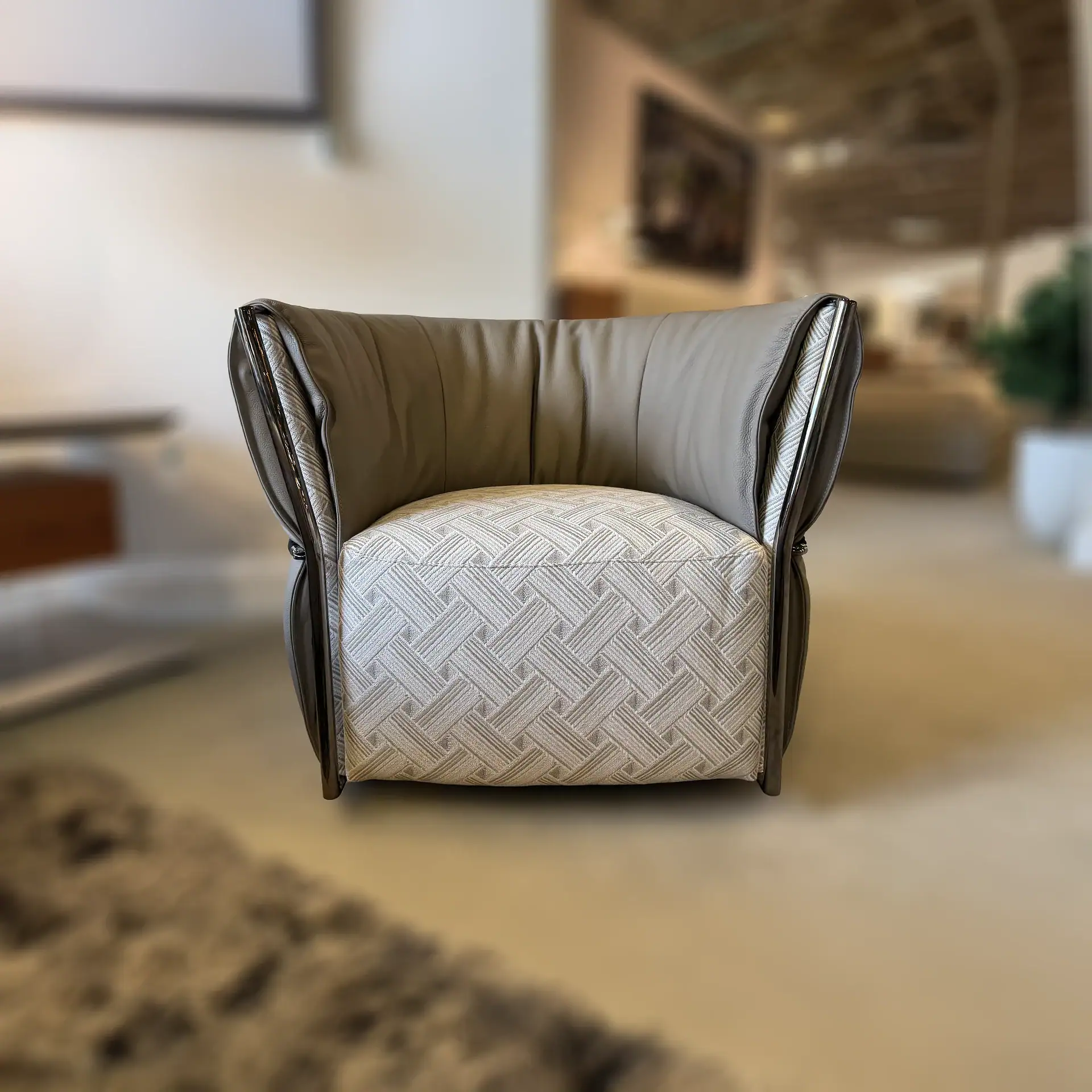 A modern armchair with taupe leather-like exterior and a light beige geometric patterned fabric on the seat and inner back, featuring dark metallic trim.