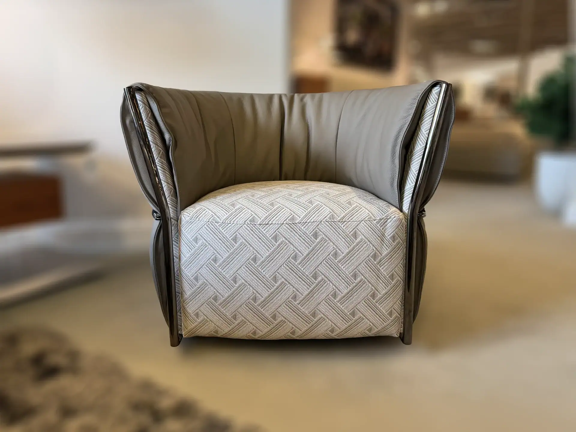 A modern armchair with a light geometric patterned seat and dark grayish-brown leather back and armrests, featuring dark trim.