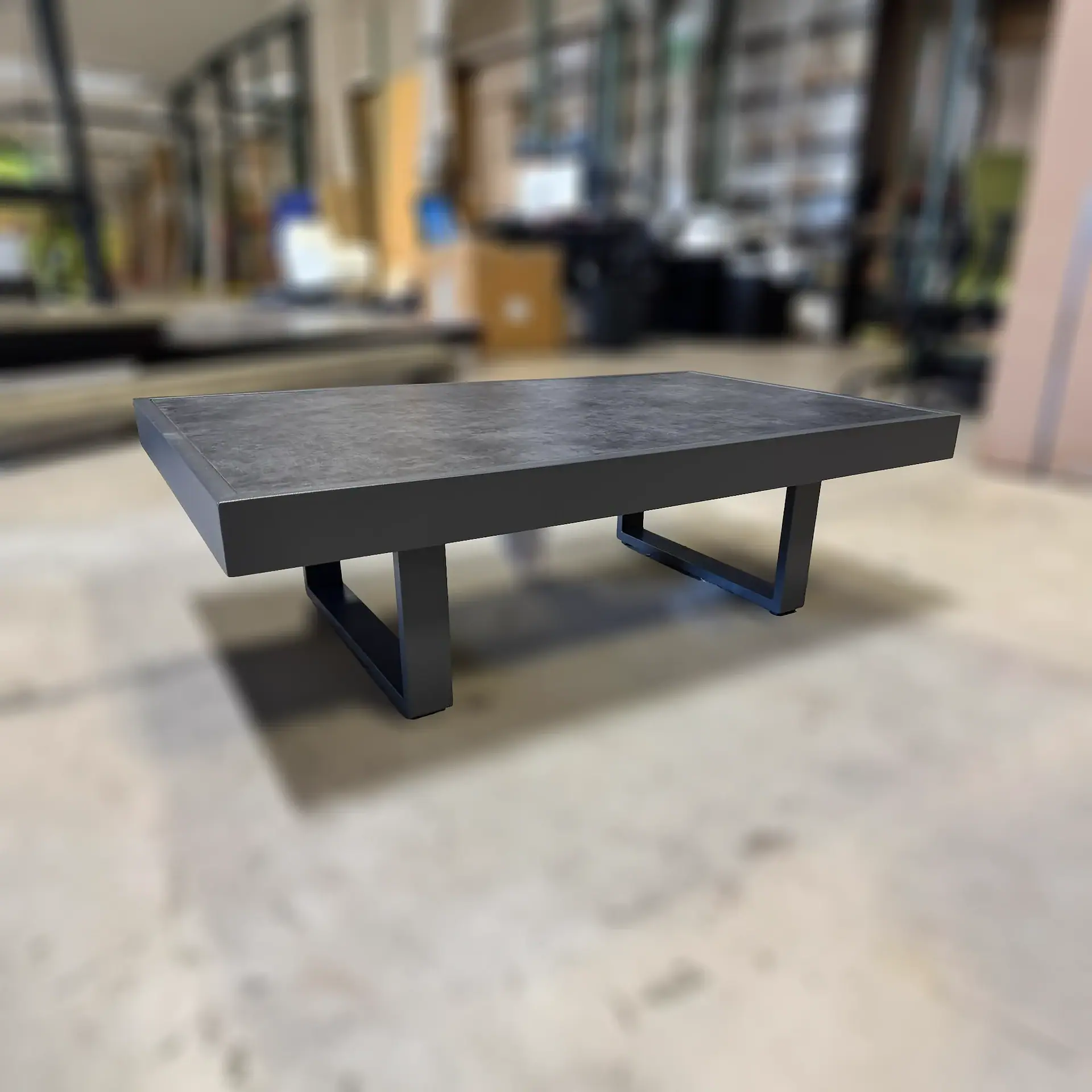 A rectangular coffee table with a dark gray textured top and black metal U-shaped legs, set against a blurred indoor background.