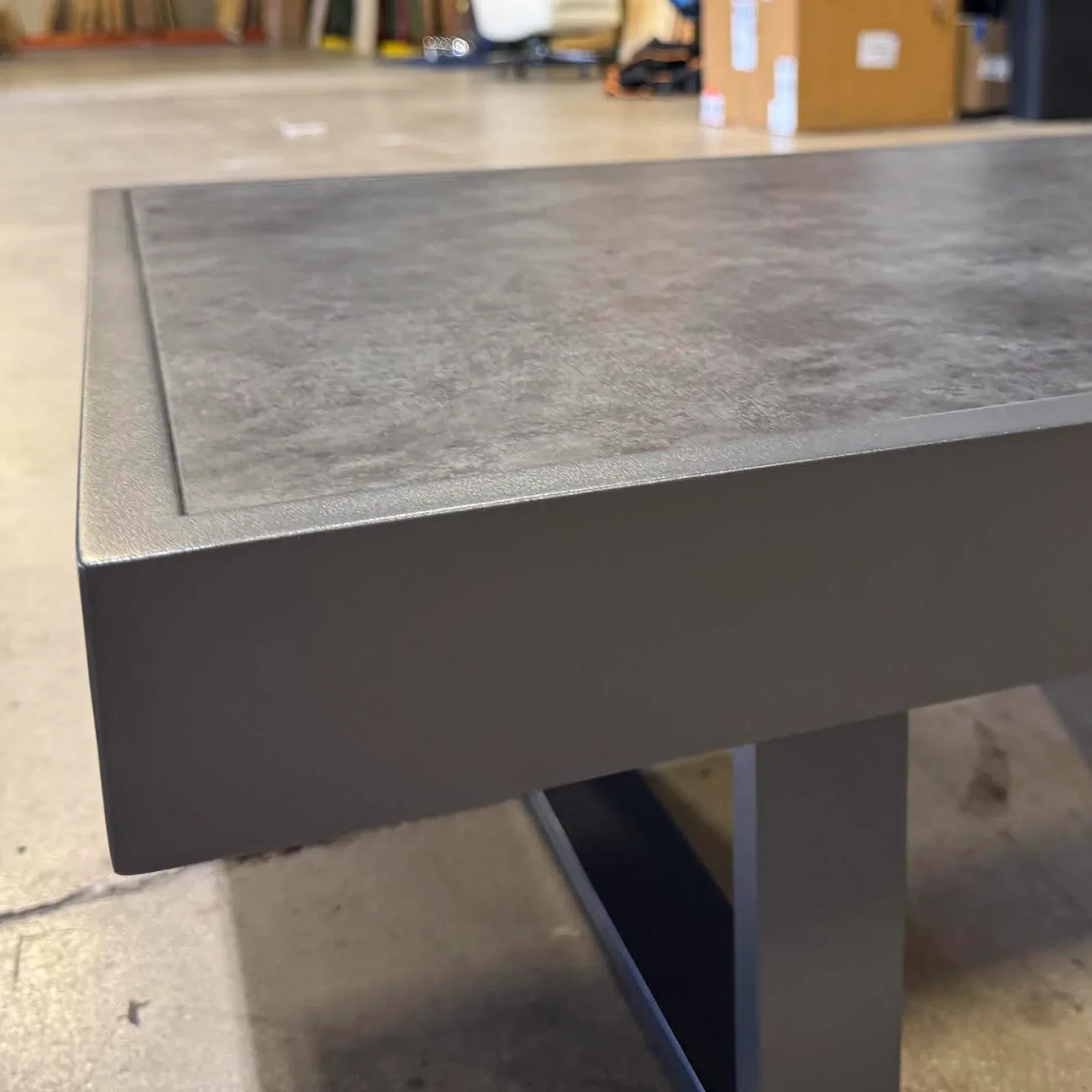 Close-up of a dark gray table corner with a textured, recessed top and a matte frame.
