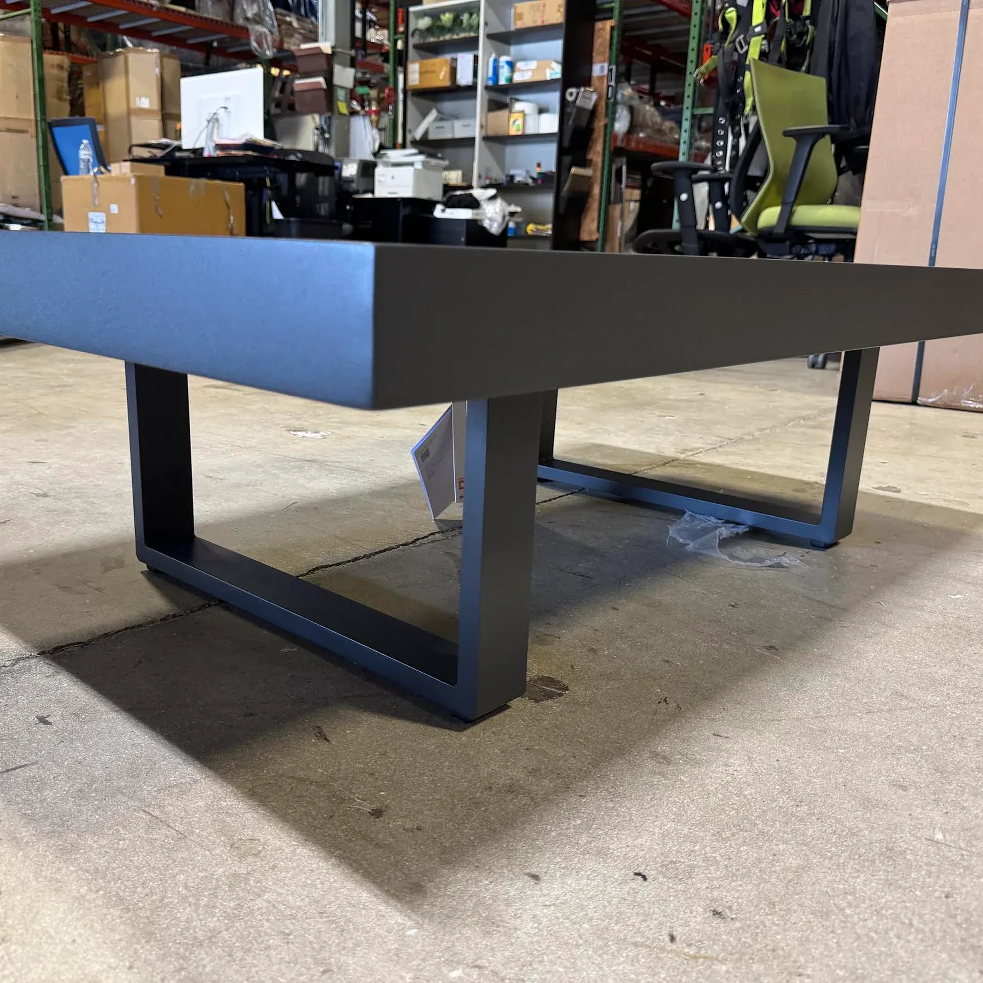A dark gray rectangular coffee table with U-shaped legs on a concrete floor in a warehouse setting.