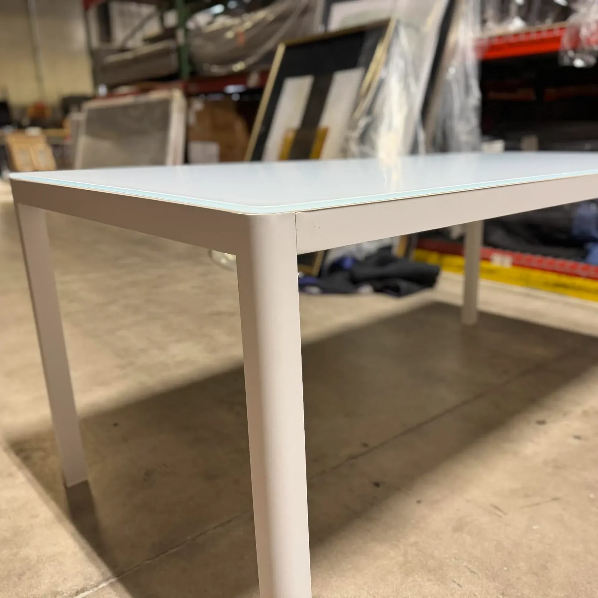 Sklar outdoor dining table with white frame and light glass top.