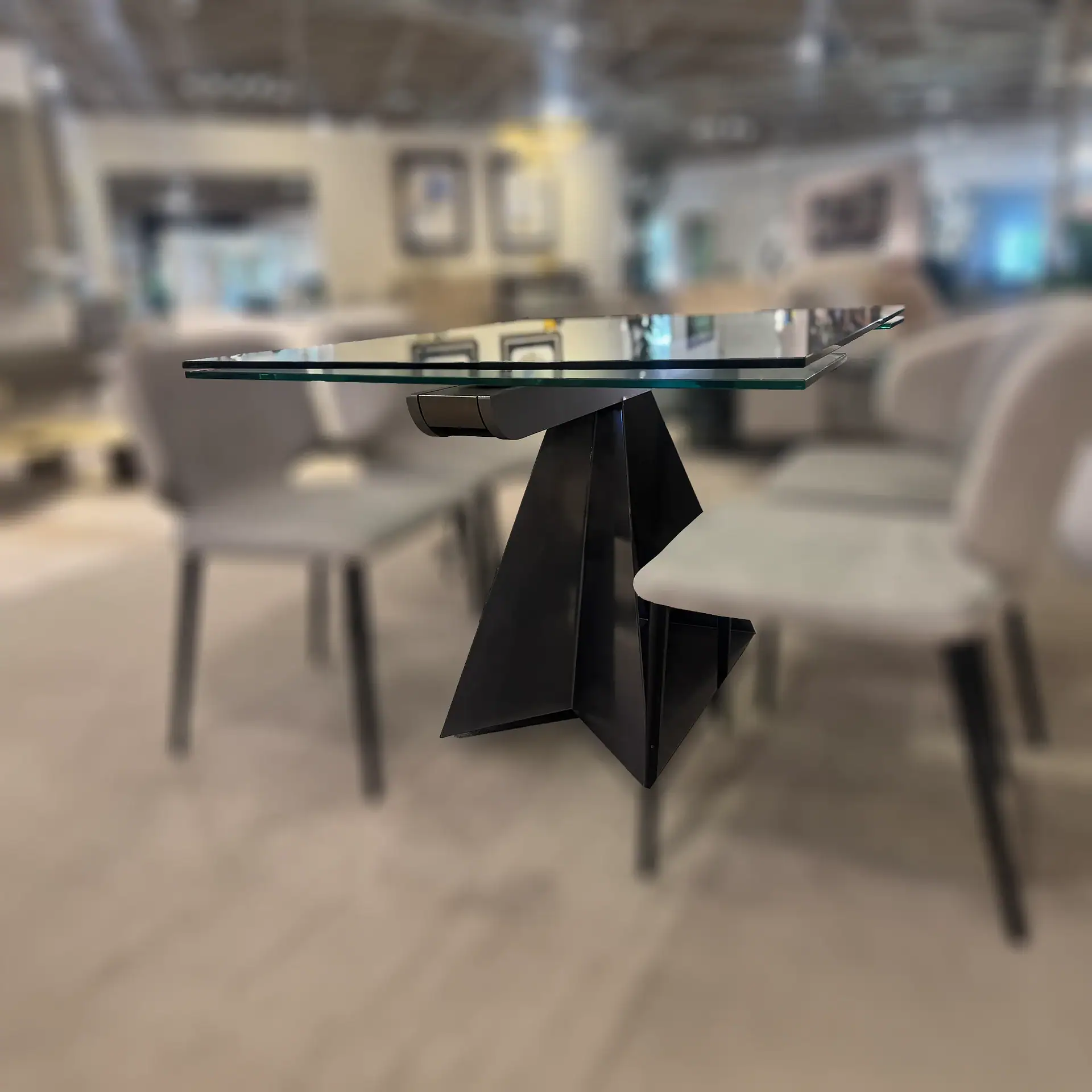 Modern dining table with a layered glass top and a black, geometric, sculptural base, with two light chairs.