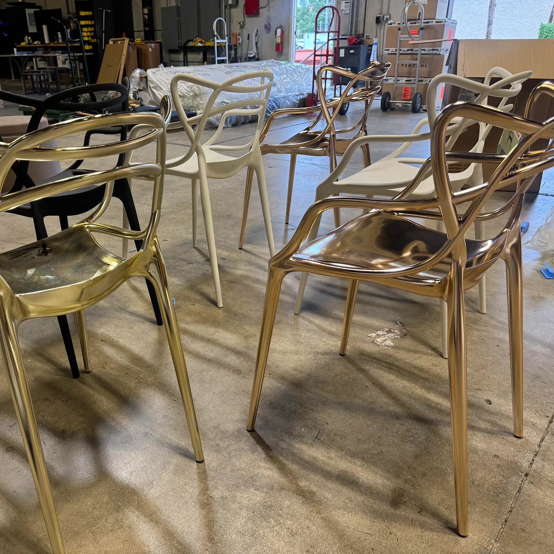 Modern chairs in gold, white, black, and rose gold on a concrete floor in a warehouse.