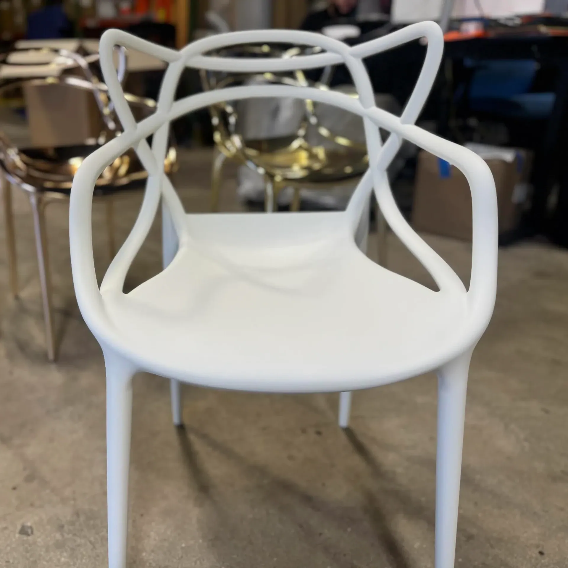 A white modern chair with a sculptural, looped backrest and armrests, on a concrete floor.