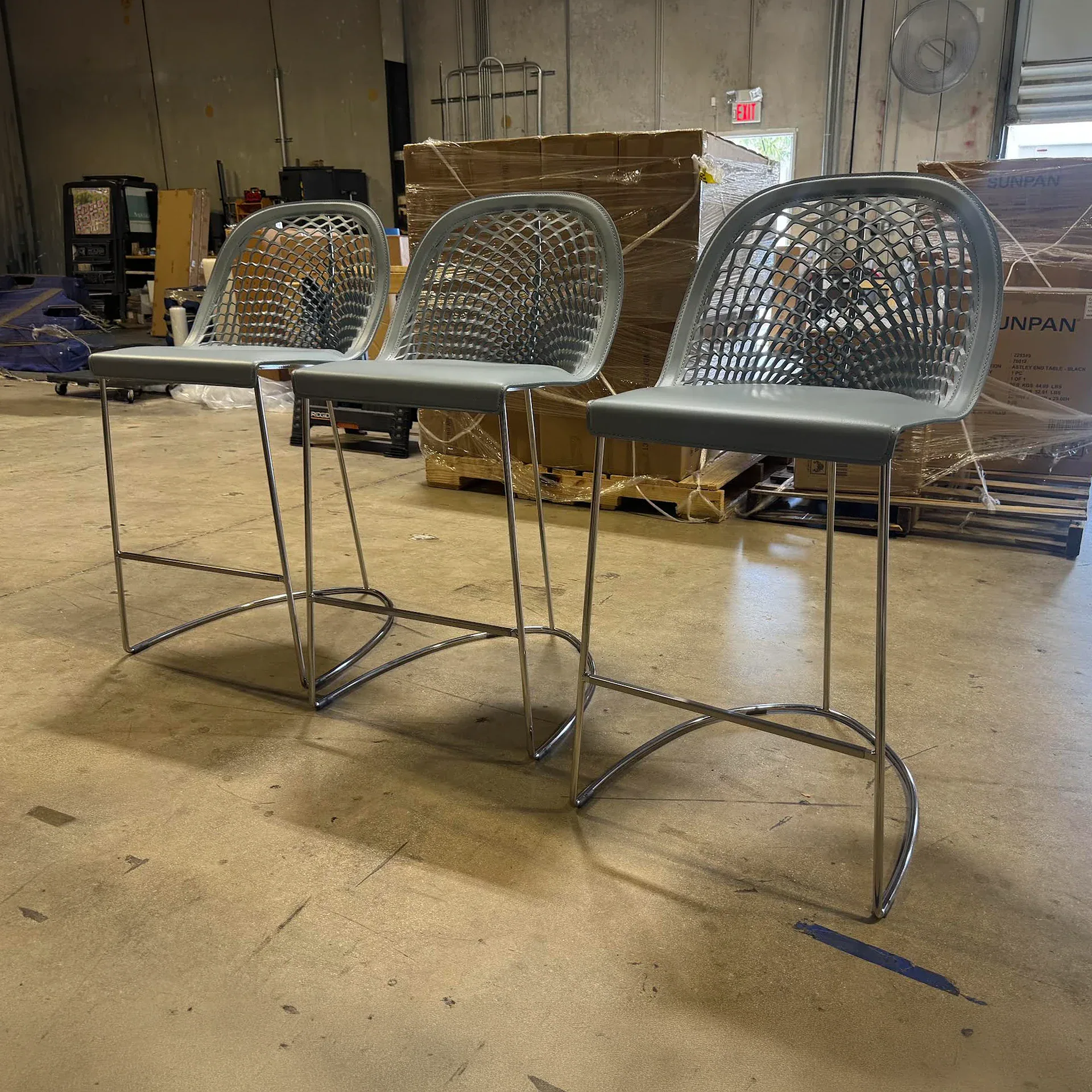 Sklar Furnishings stool trio with metal frame and perforated backrests in an industrial setting.