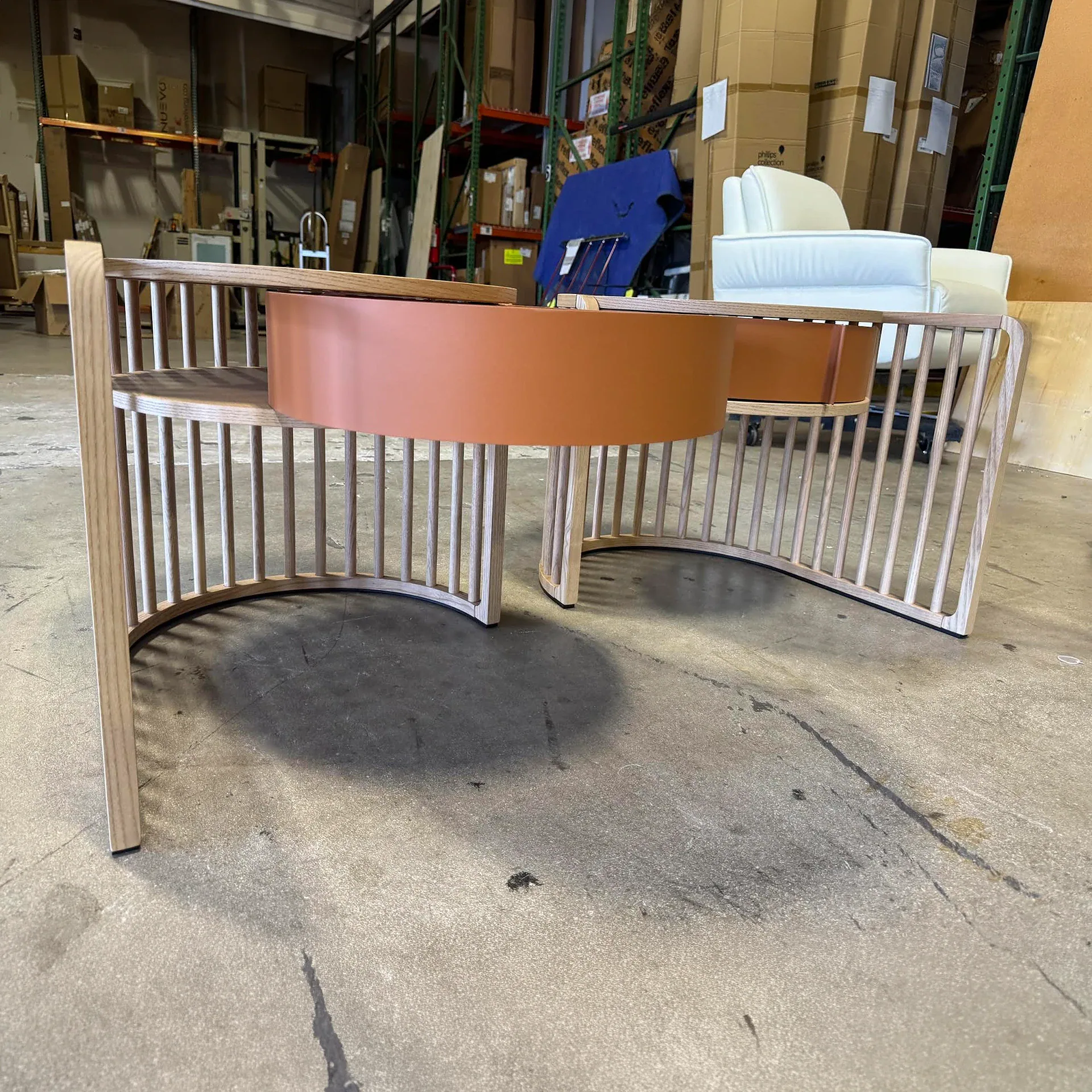 A modern furniture piece with light wood slats and a central terracotta-colored planter, set against a warehouse background.