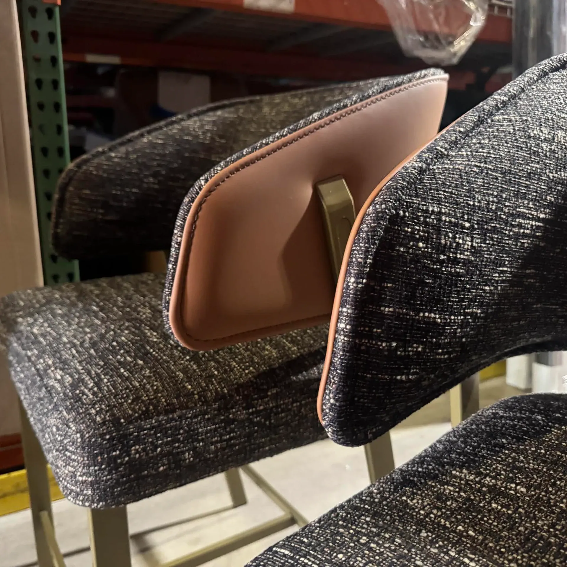Close-up of dark textured fabric chairs with light brown leather accents and metal frames, set against a blurred warehouse background.