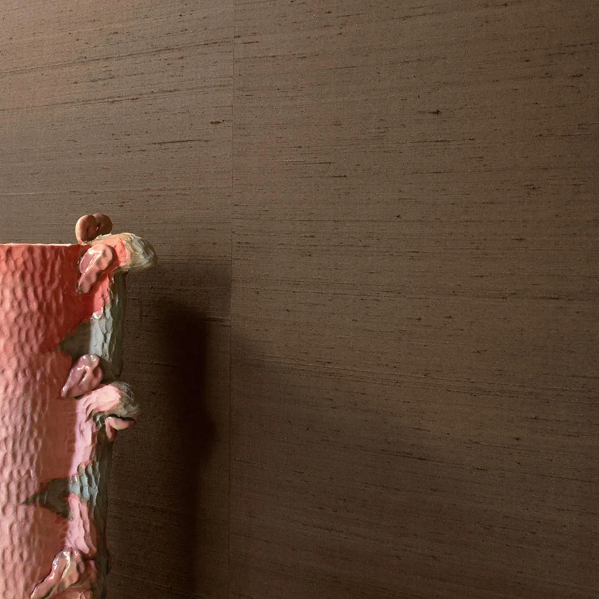 Sklar Furnishings wallpaper roll with textured pink floral edge against brown wall.