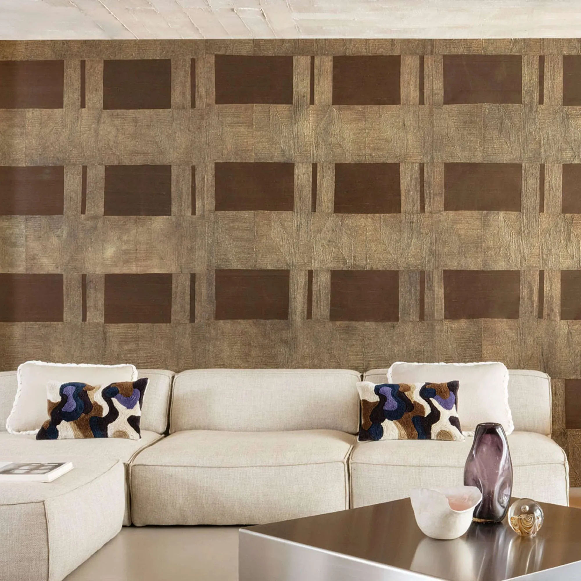 Sklar Furnishings beige sectional with patterned pillows in front of geometric wallpaper.