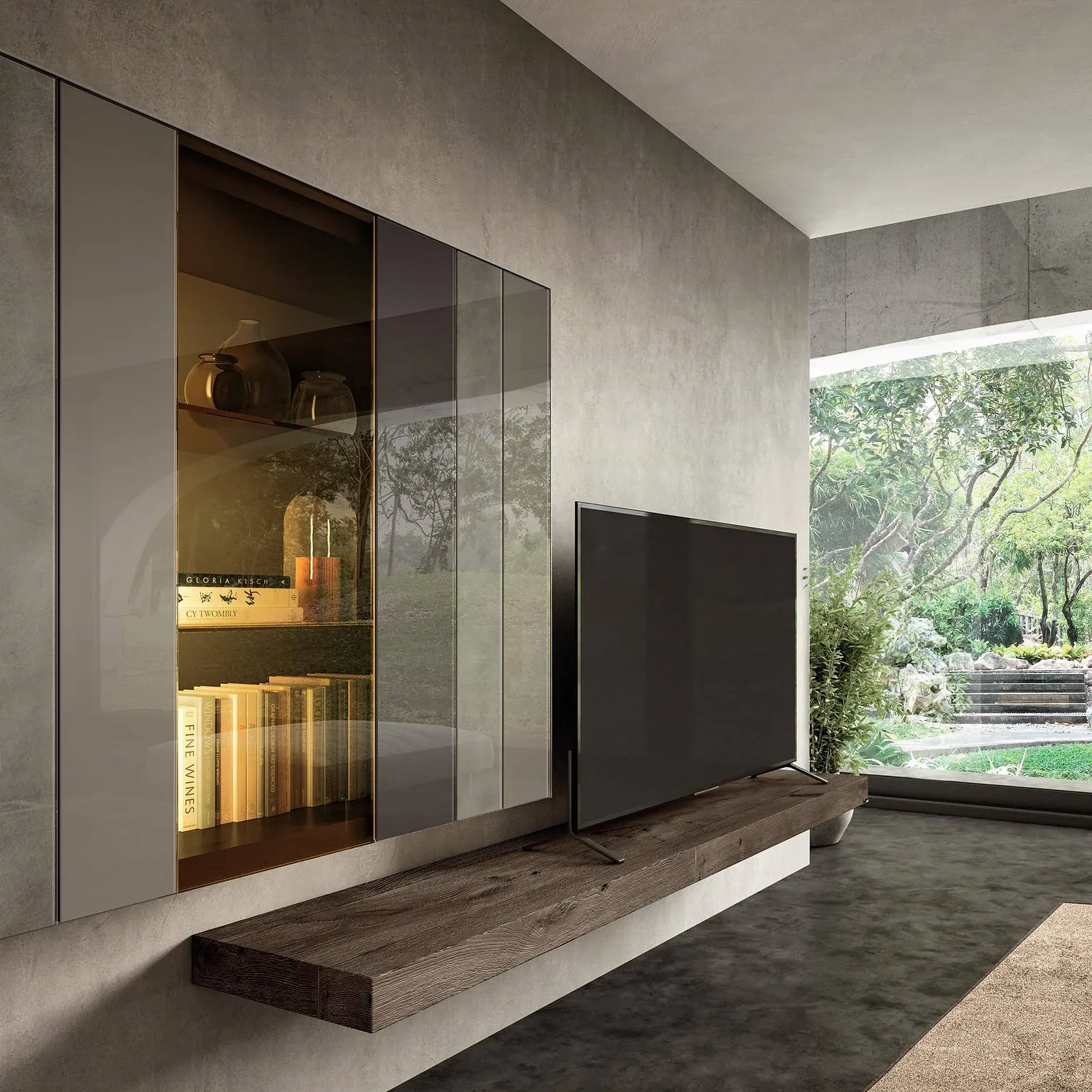 A modern living room with concrete walls, a built-in glass cabinet displaying books and vases, a large TV on a floating dark wood shelf, and a window overlooking a lush green garden.