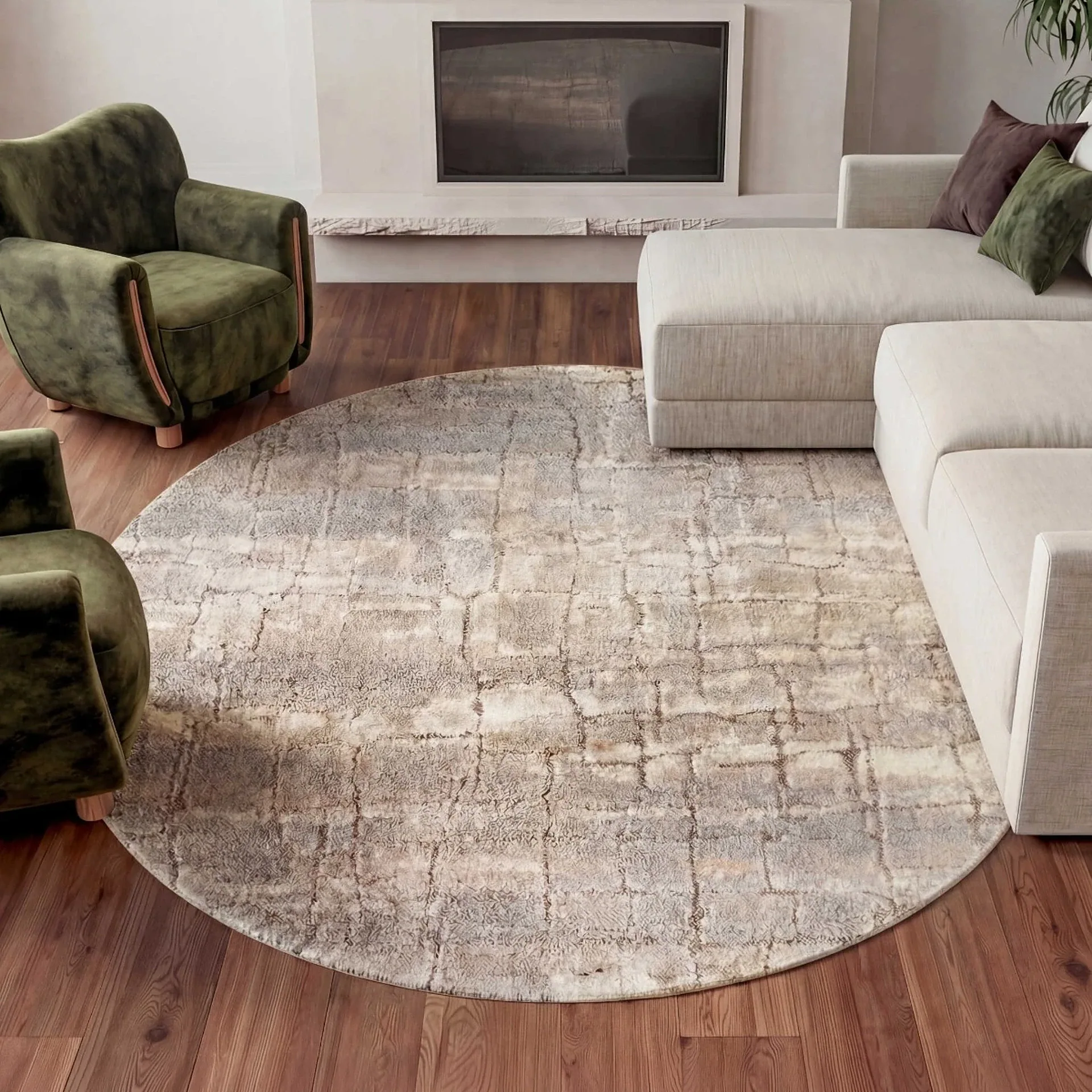 A modern living room with a round patterned rug, two green velvet armchairs, a beige sectional sofa with pillows, and a fireplace.