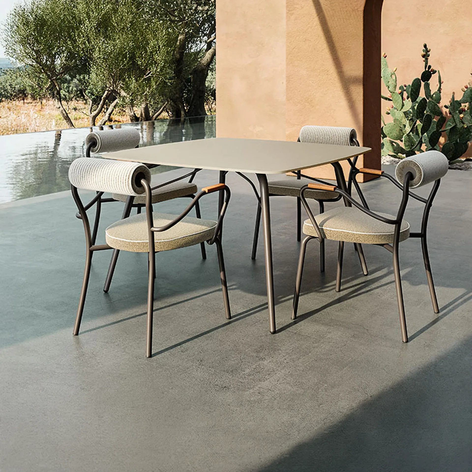 An outdoor dining set with a square table and four chairs on a patio next to a pool and a terracotta wall with cacti.