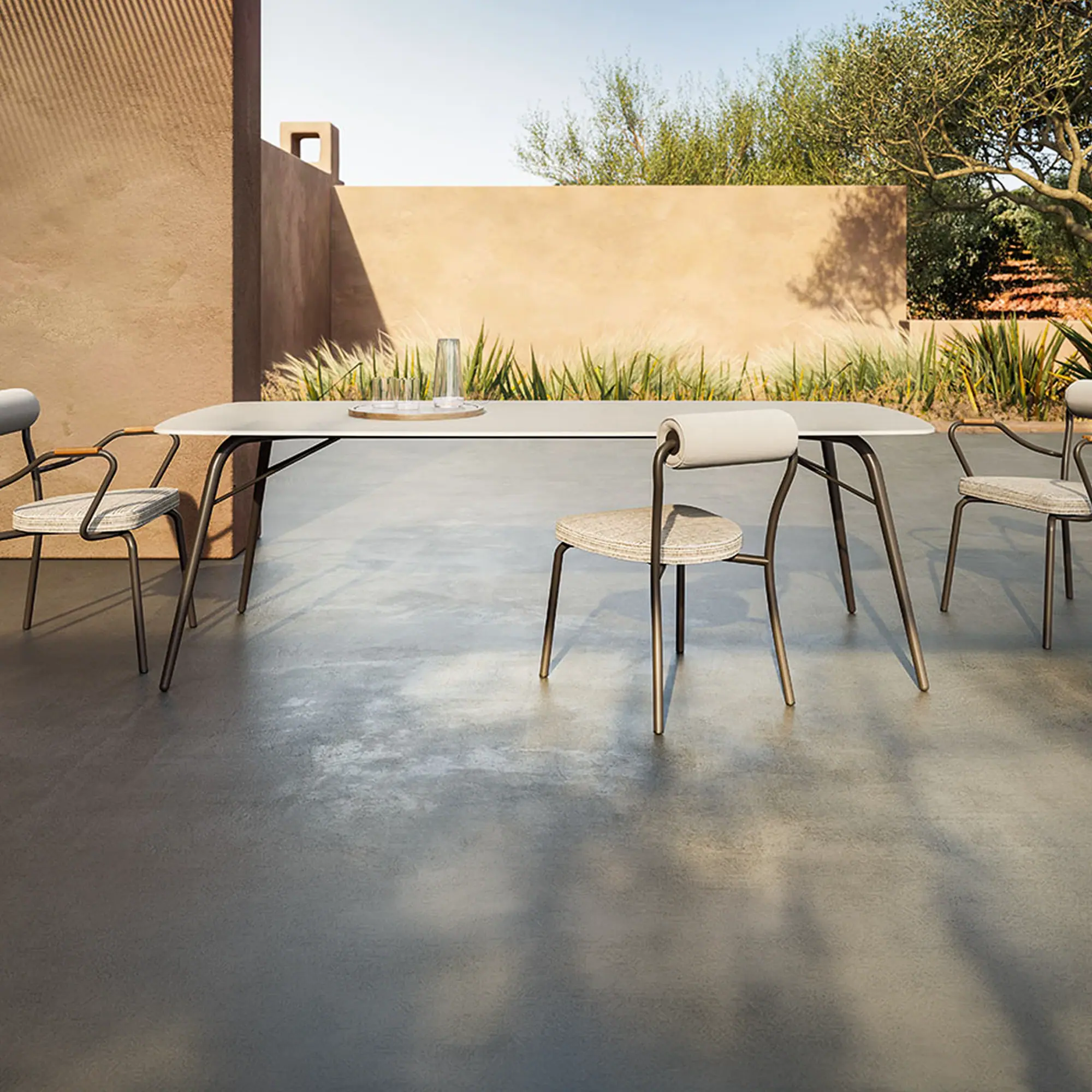 A modern outdoor dining set with a rectangular table and four chairs on a concrete patio, surrounded by stucco walls and green plants under a clear sky.
