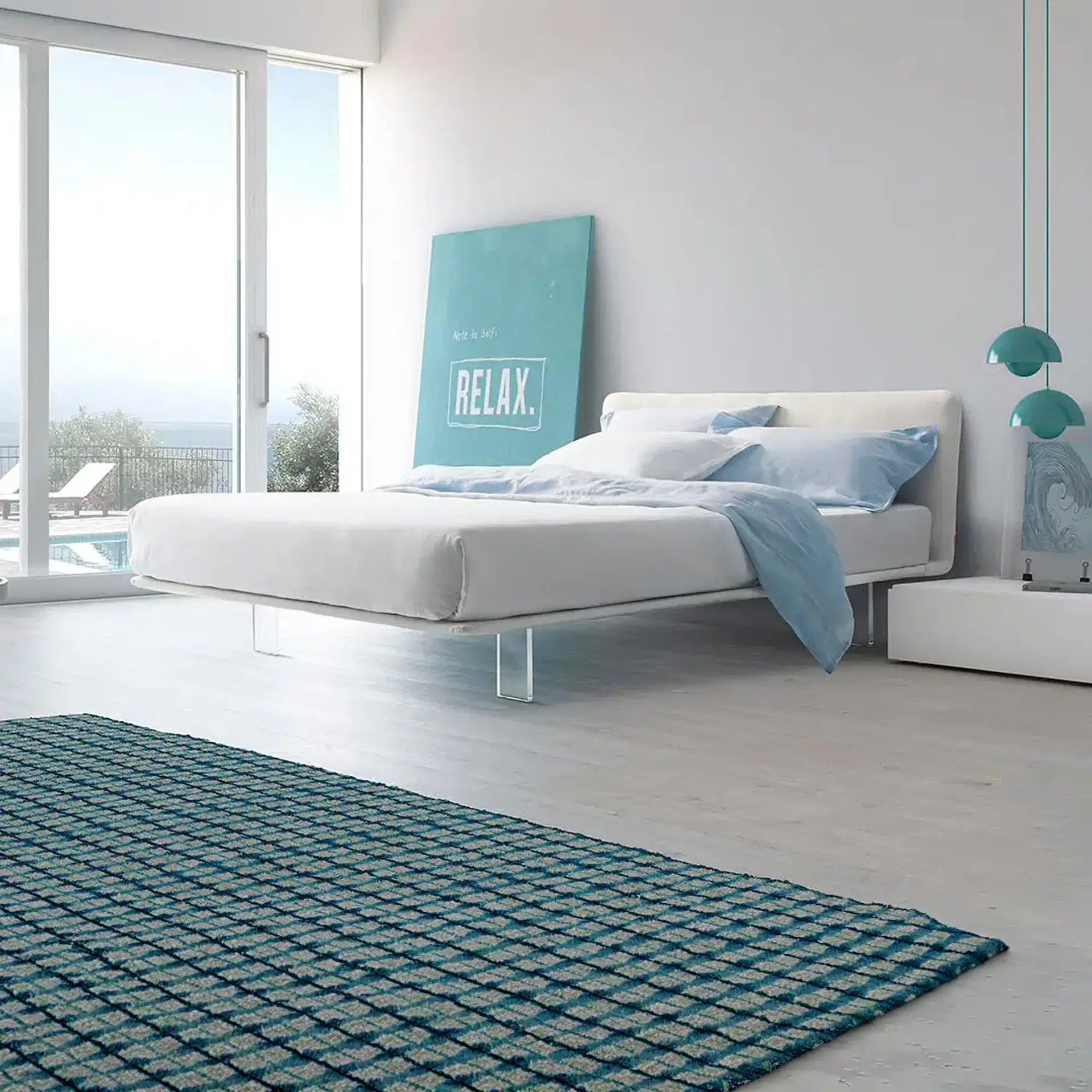 A modern bedroom with a white bed, light blue bedding, and a large window overlooking a pool and ocean. A teal rug is in the foreground.