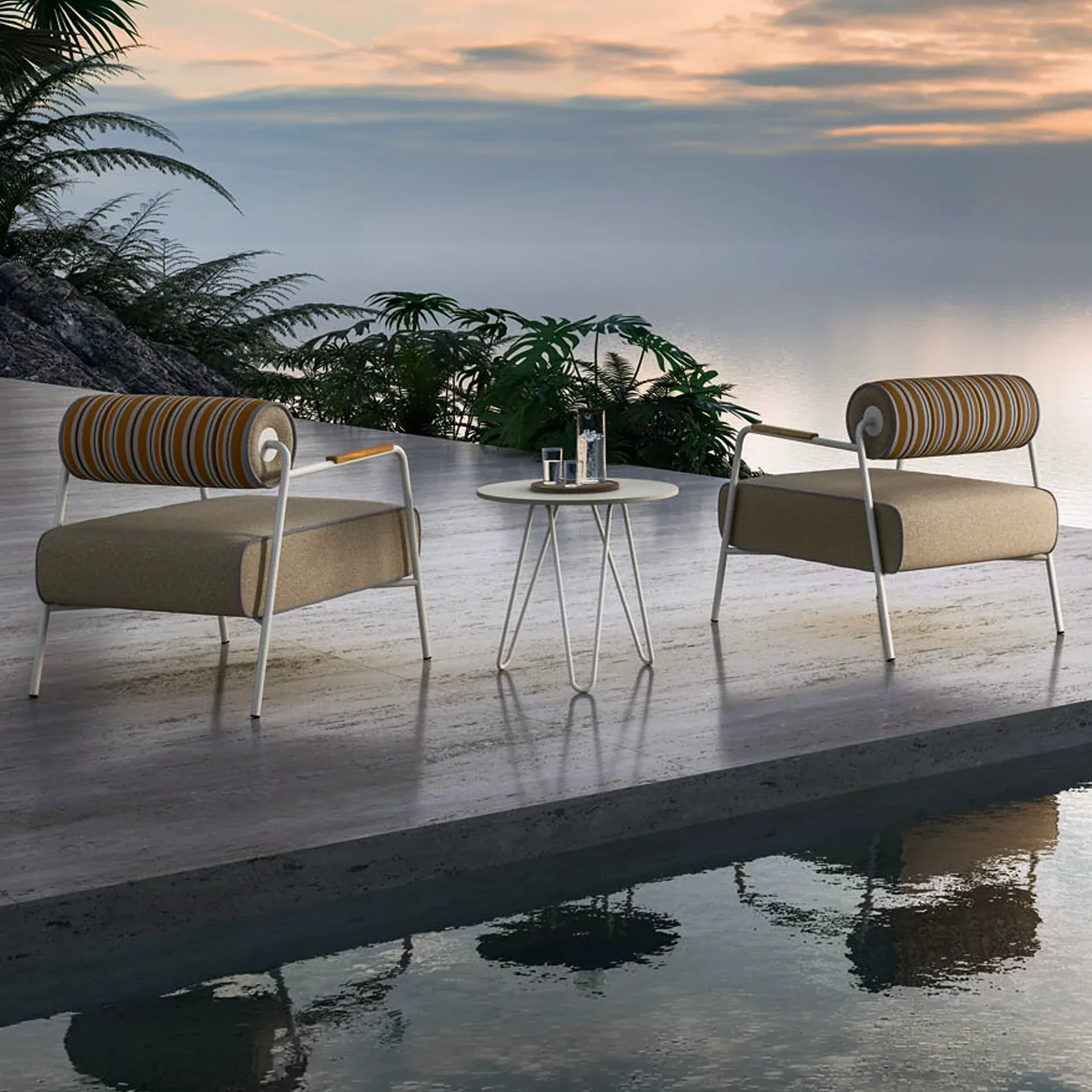 Two modern outdoor lounge chairs with striped backrests and a white side table on a concrete patio overlooking water at sunset.