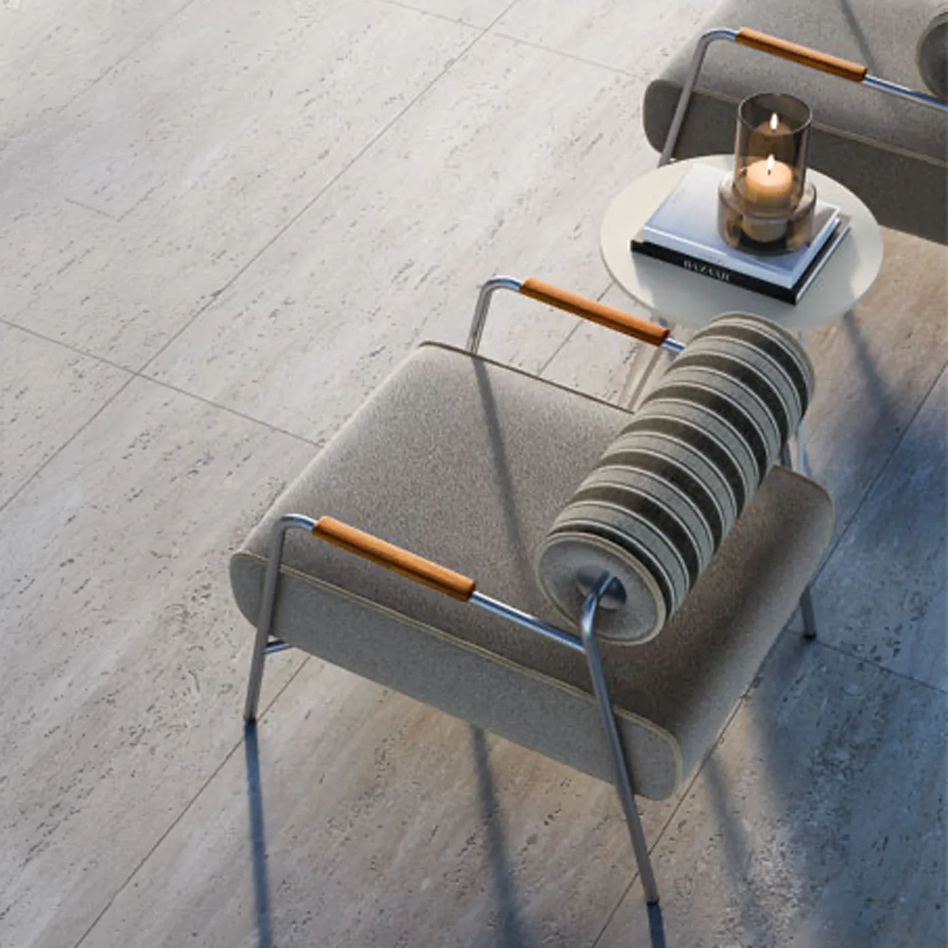 High-angle view of two modern gray armchairs with chrome frames and wooden armrests, flanking a white side table. The table holds two stacked books and a glass candle holder with two lit candles, all on a light gray tiled floor.