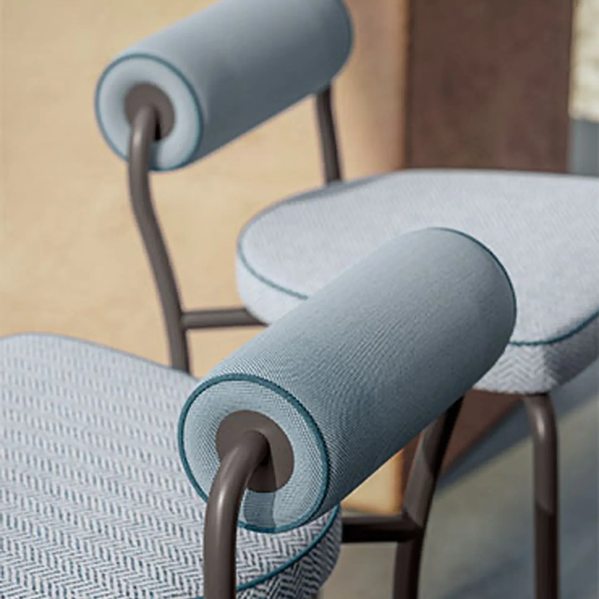 Close-up of two modern chairs with light blue herringbone seats, cylindrical blue backrests, and dark metal frames.