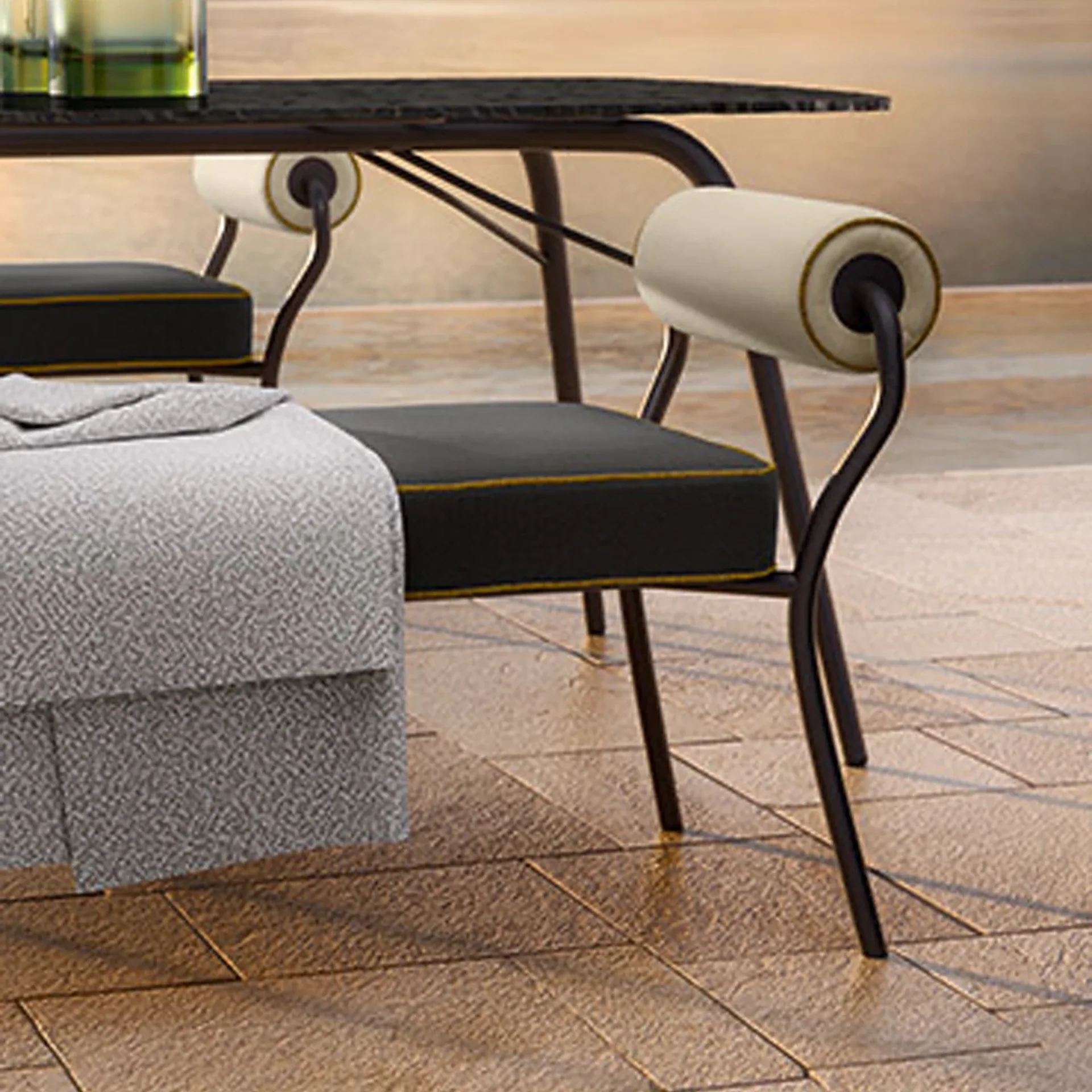 Close-up of modern outdoor chairs with dark frames, cream armrests, and dark gray cushions with gold piping, next to a table on textured light brown tiles.